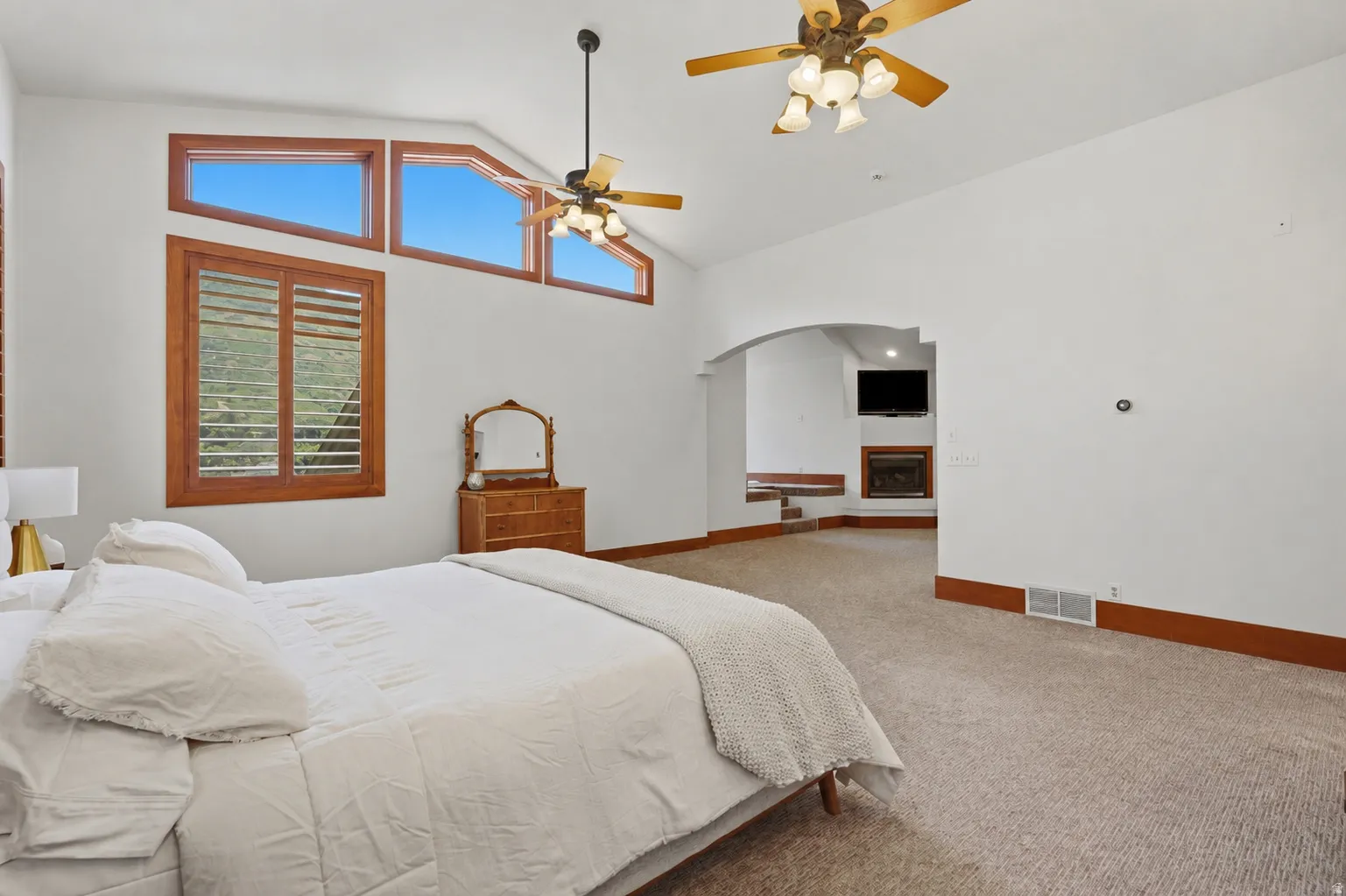 Carpeted interior space featuring a vaulted ceiling with multiple ceiling fans