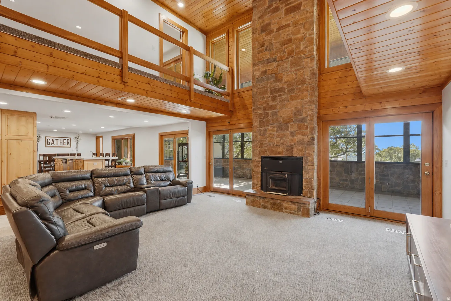 Great room featuring a floor-to-ceiling stone fireplace, high wood-paneled ceilings, and multiple sets of glass doors opening to the sunroom