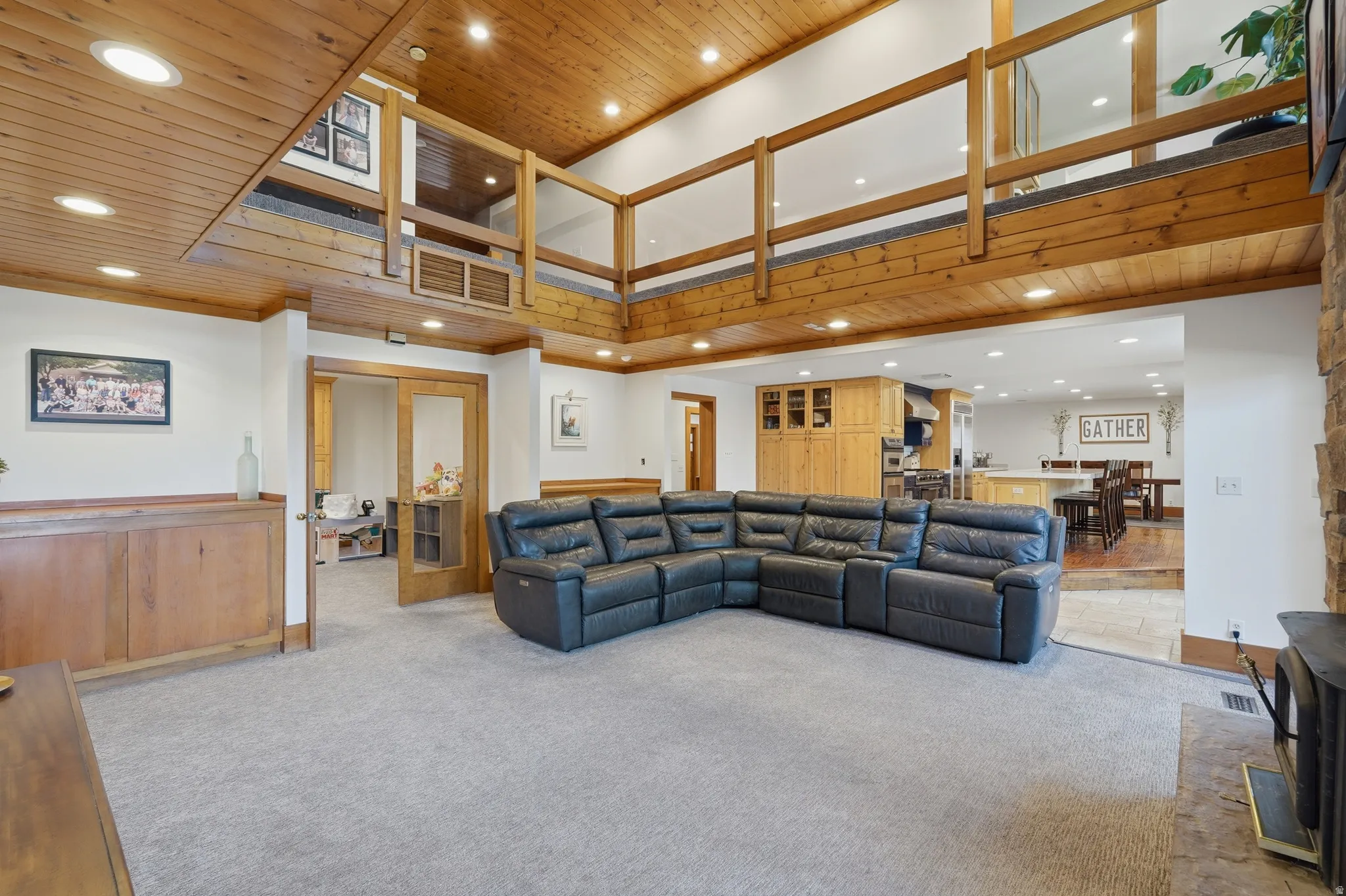 Great room featuring a vaulted wood-paneled ceiling, open loft area with wood railings, recessed lighting, and a stacked stone fireplace with a fireplace
