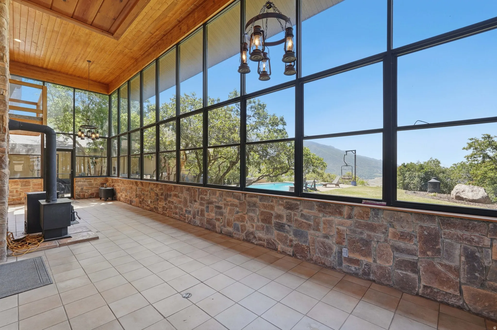 Expansive sunroom featuring floor-to-ceiling windows, stone wall accents, wood ceiling, and tile flooring