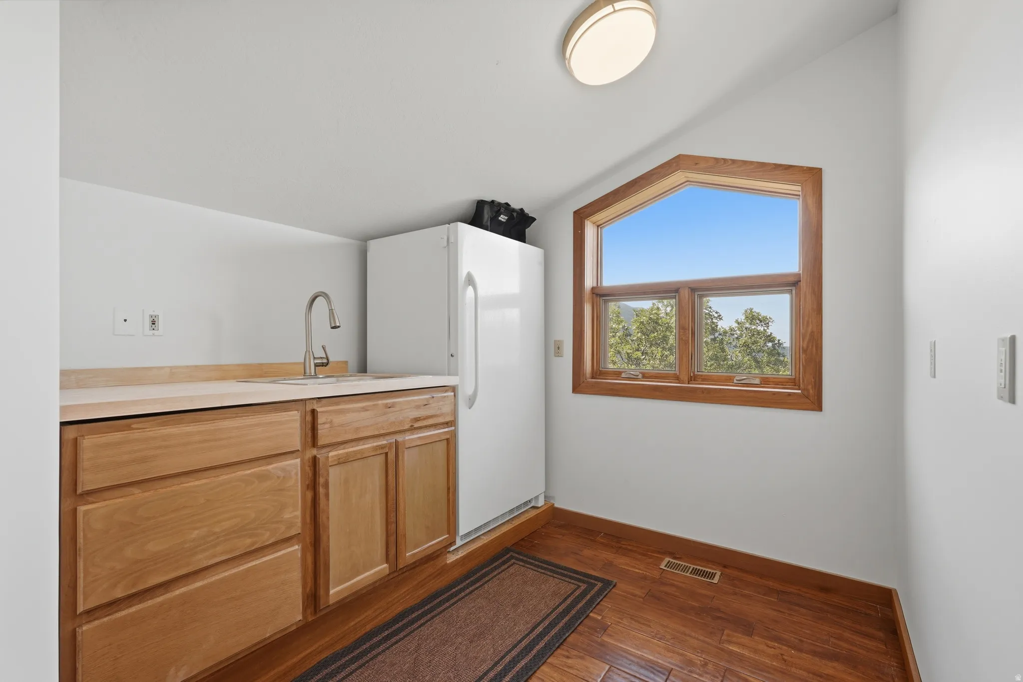 Wet bar for pool area, windowed utility area featuring wood flooring, light wood cabinetry, a sink with a gooseneck faucet, and a contemporary ceiling light fixture