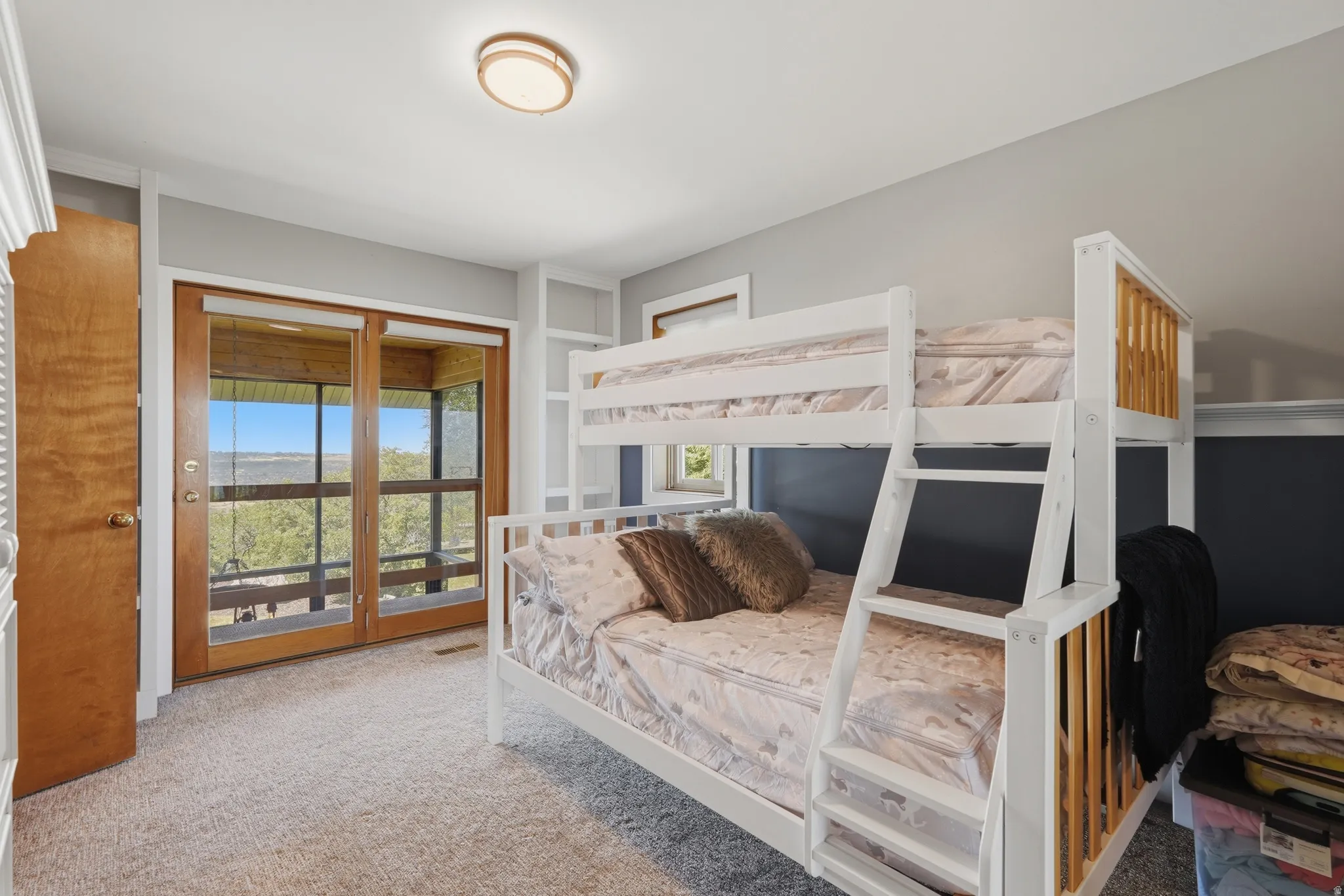 Room featuring light gray walls, plush carpeting, a ceiling-mounted light fixture, and built-in shelving, and a balcony with entrance to the sunroom