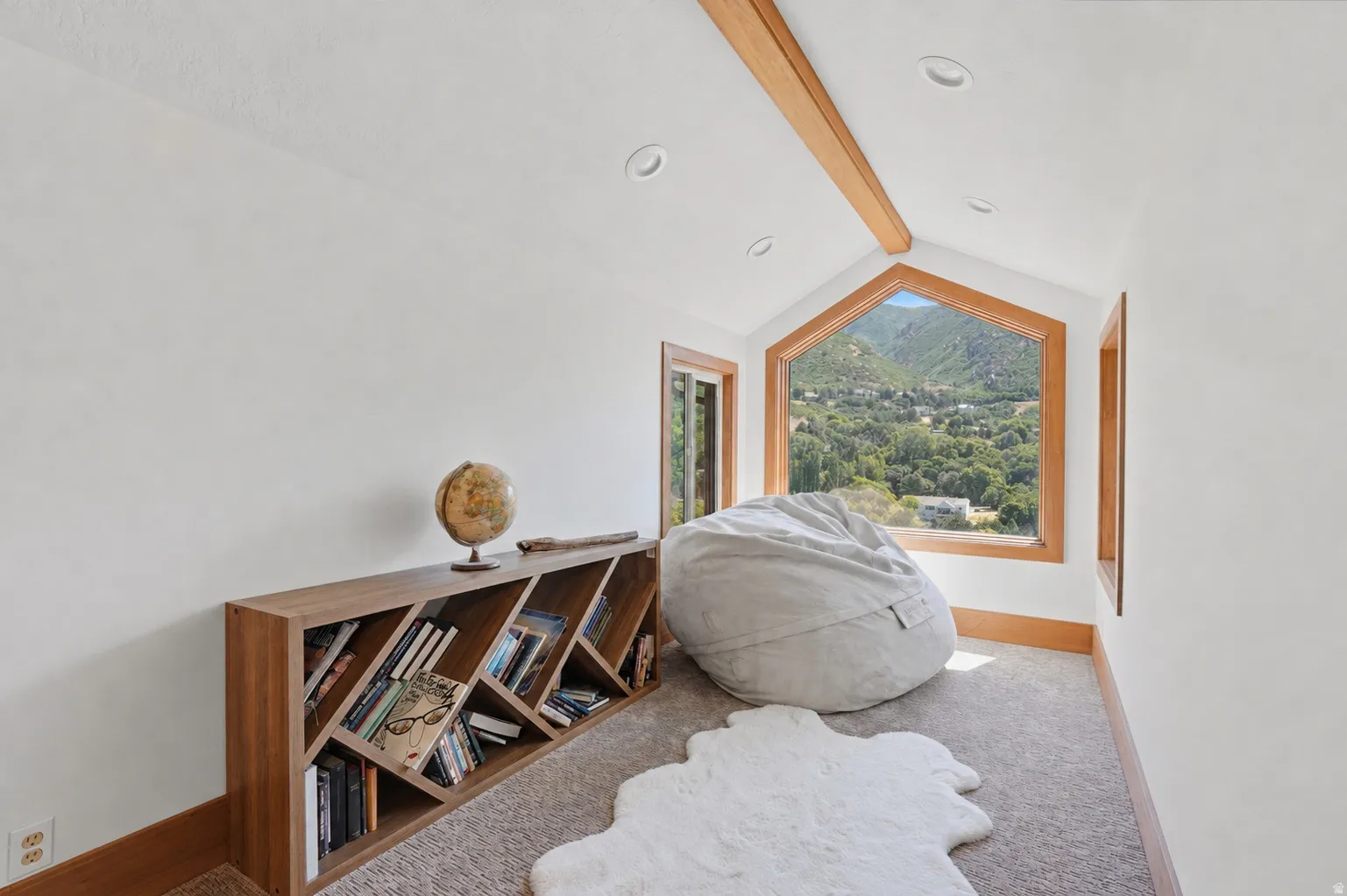 Vaulted ceiling with exposed wood beams, recessed lighting, and a large trapezoidal window with a natural wood frame