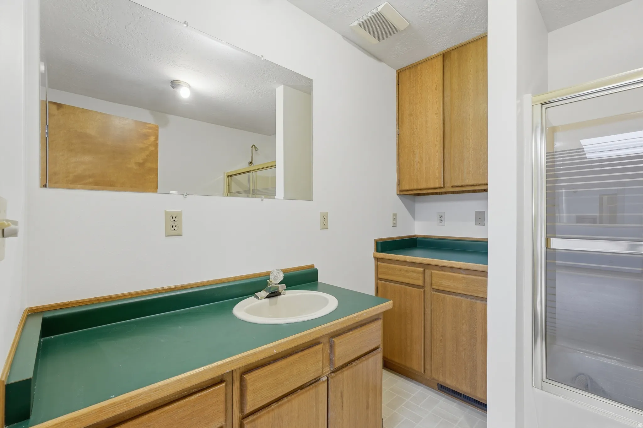 Bathroom vanity with an integrated sink and green countertop, complemented by light wood-finish cabinetry