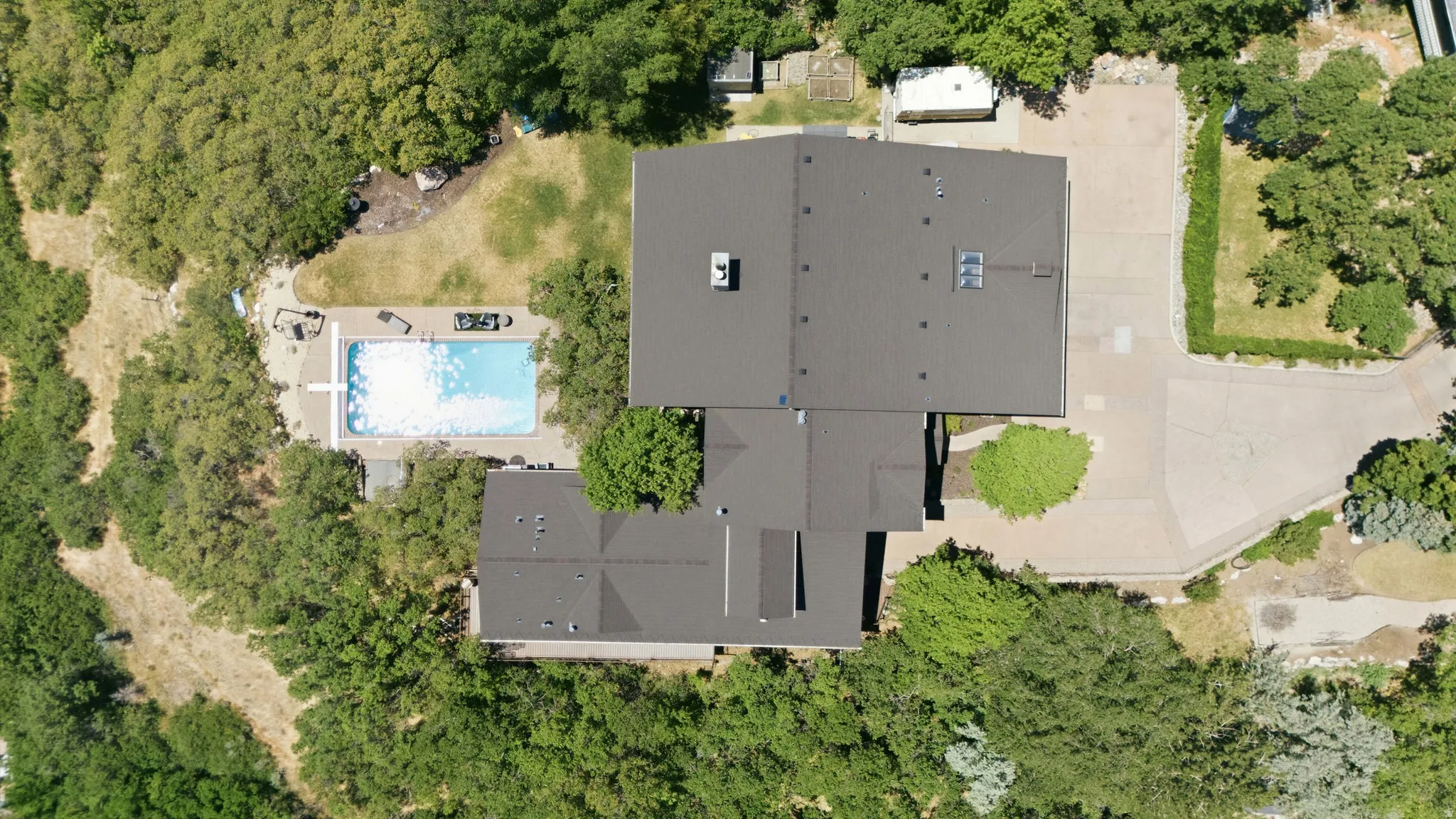 Expansive property featuring a multi-structure layout with dark gray roofing, a large inground swimming pool, and extensive surrounding greenery