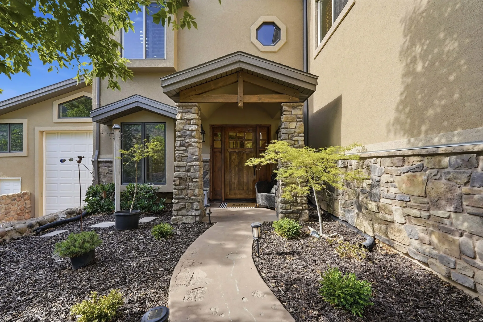 Stone and stucco exterior featuring a covered entry, wood-paneled door, octagonal window, and a curved pathway