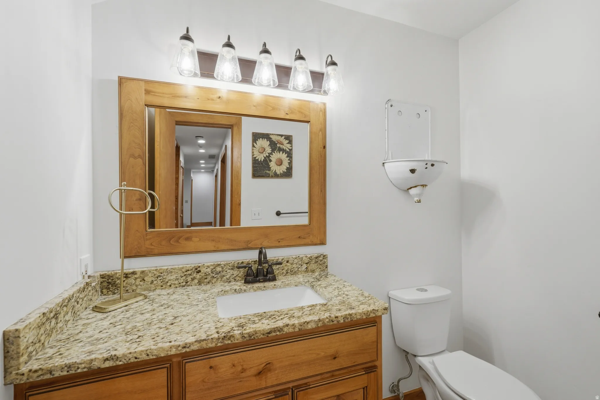 Half bath with a vanity featuring a light wood-finish frame mirror, a light granite countertop, and wood-finish cabinetry