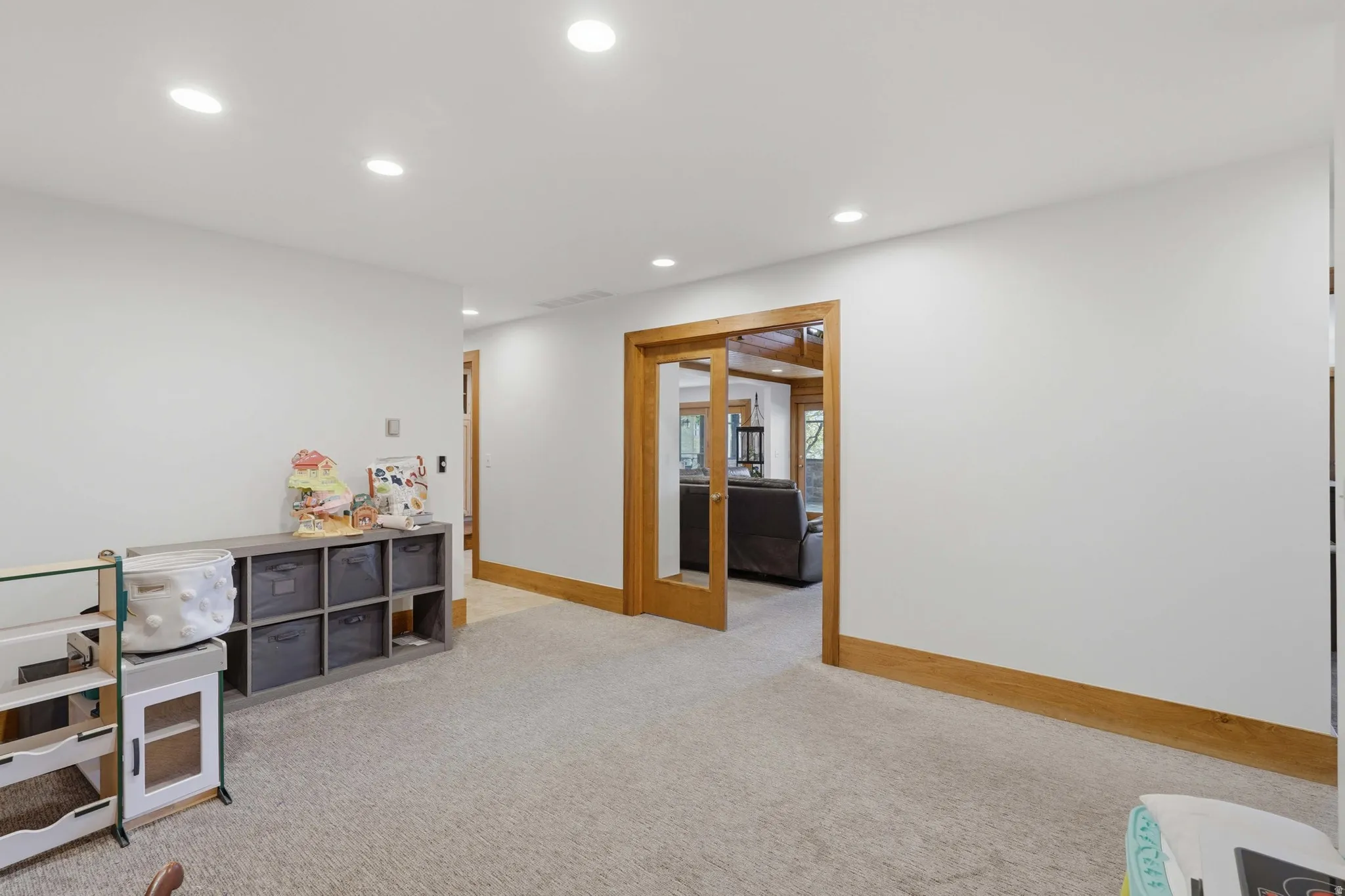 Spacious room featuring light-toned carpeting, recessed ceiling lighting, and white walls with natural wood trim