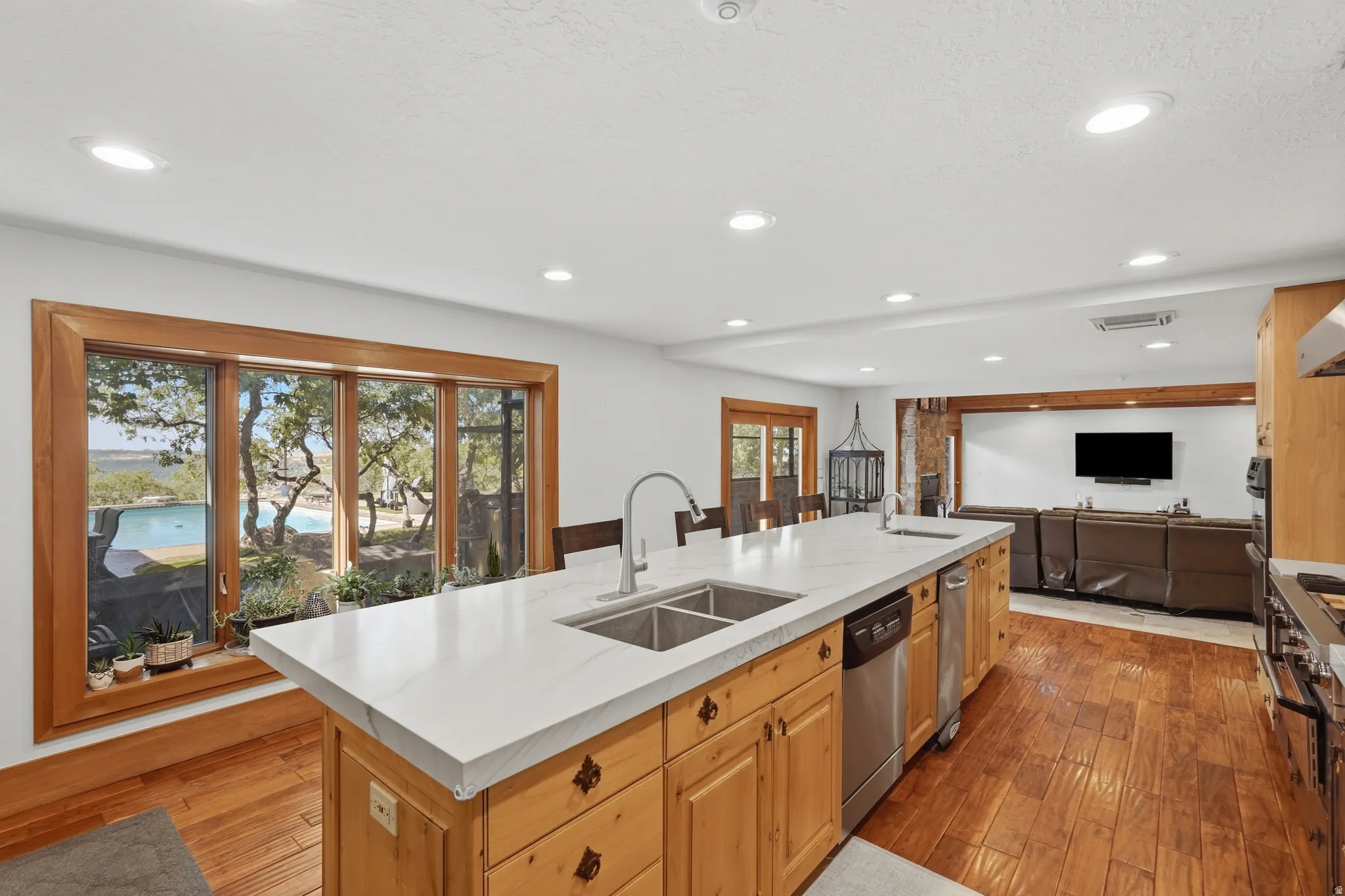 Spacious kitchen overlooking the swimming pool, featuring a large central island with a double basin sink, white countertops, and wood cabinetry