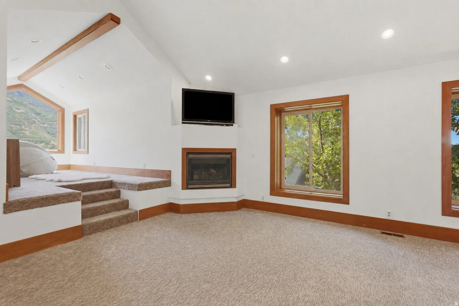 Carpeted room featuring a built-in corner fireplace, recessed lighting, and wood-trimmed windows