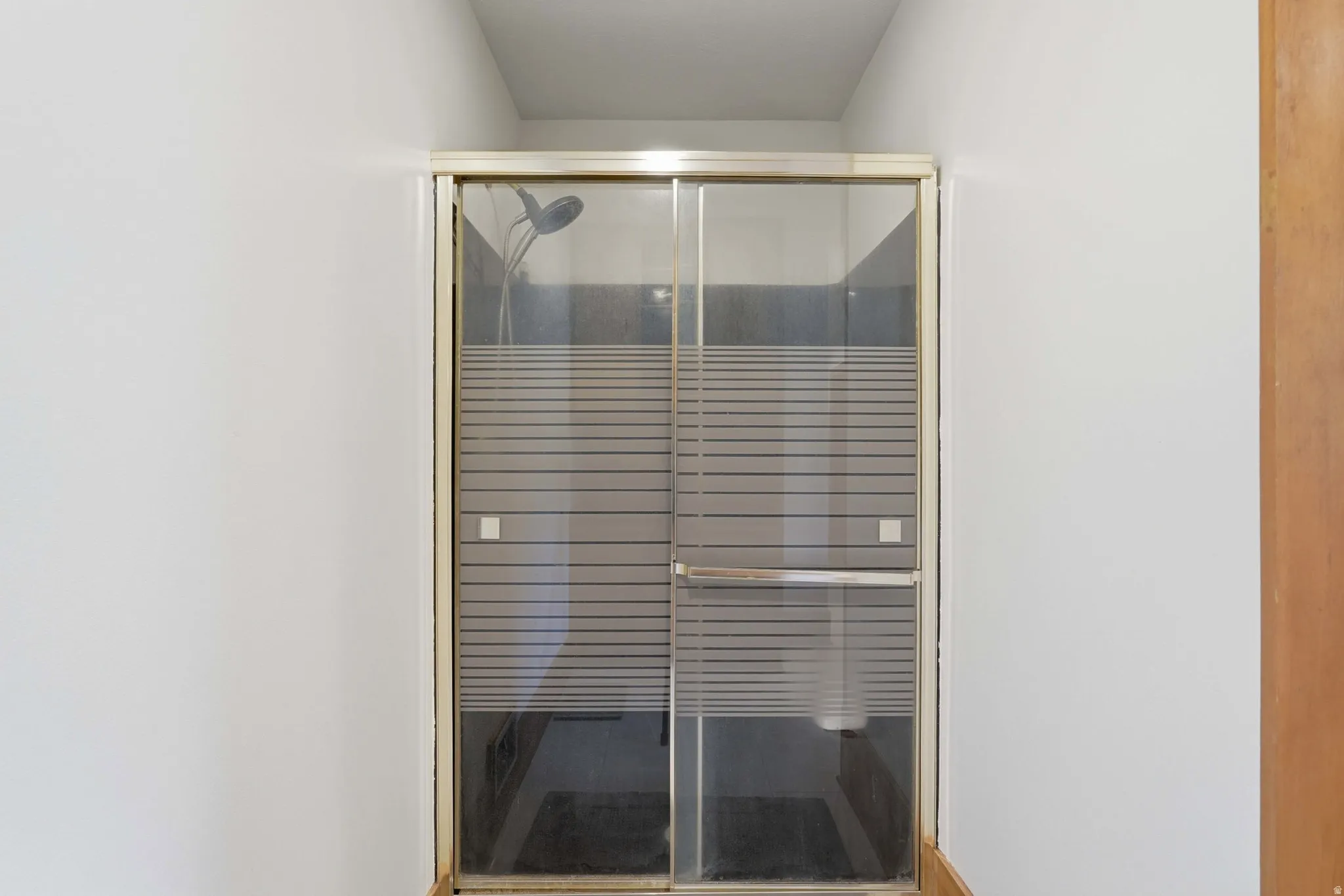 Shower enclosure with a framed sliding glass door, privacy-striped glass panels, and a chrome showerhead
