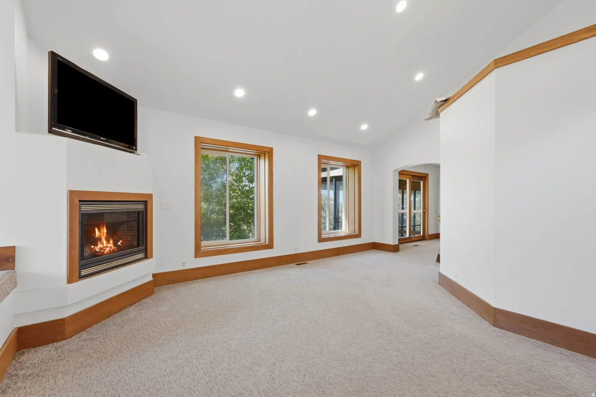 Corner fireplace with natural wood trim, recessed ceiling lighting, and light-toned carpeting
