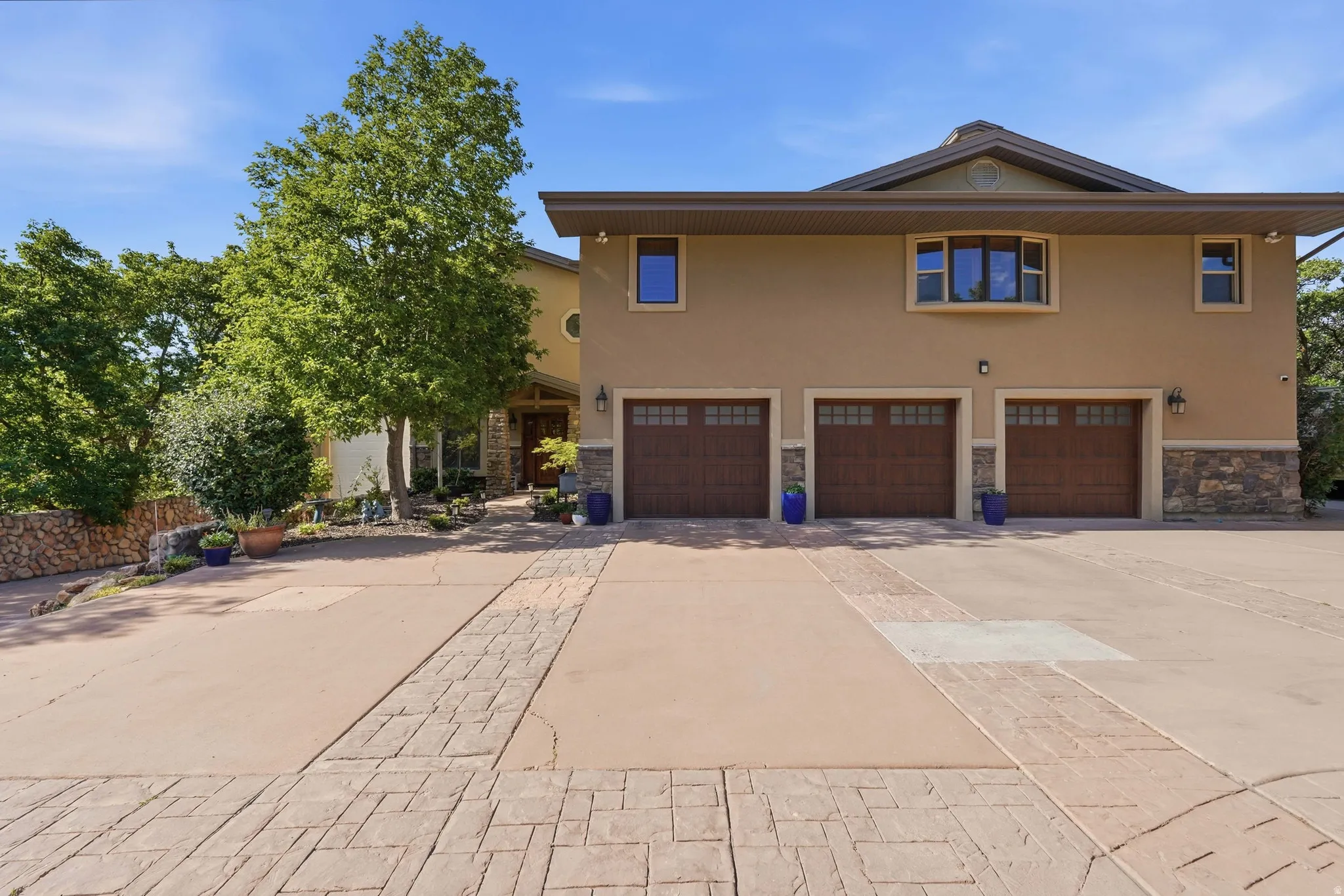 Stucco exterior featuring a three-car garage with wood-finish doors and stone accents