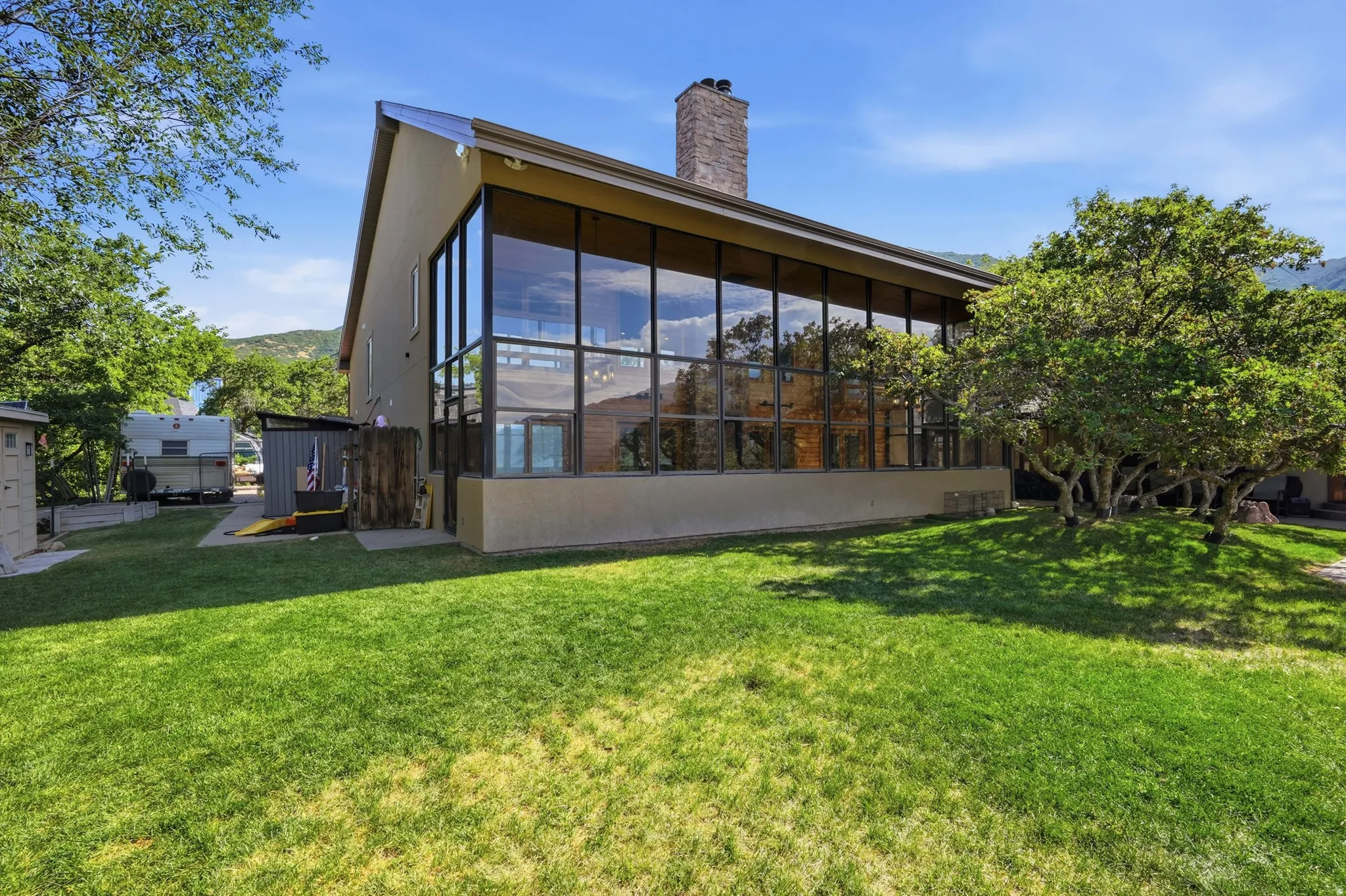 Contemporary architecture featuring a stucco exterior, a prominent stone chimney, and a full-height window wall with dark framing