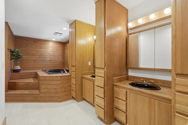 Primary bathroom with wood-paneled bathroom featuring a built-in jetted tub, stepped platform, and white tile flooring