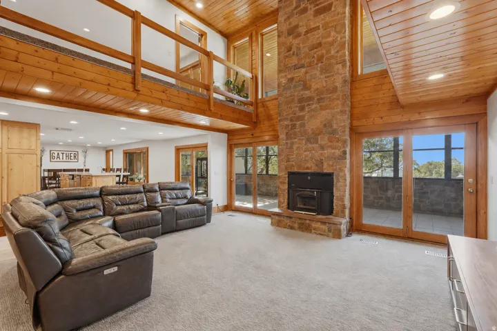 Great room featuring a floor-to-ceiling stone fireplace, high wood-paneled ceilings, and multiple sets of glass doors opening to the sunroom