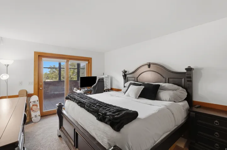Bedroom featuring carpet flooring, white walls, and a sliding glass door with wood trim opening to the sunroom