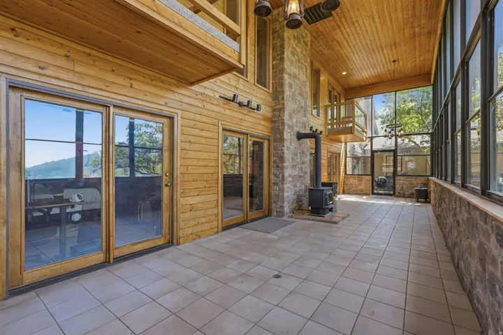 Expansive enclosed sunroom featuring a stone accent wall, wood-paneled ceiling, wood-burning stove, and extensive window-walls