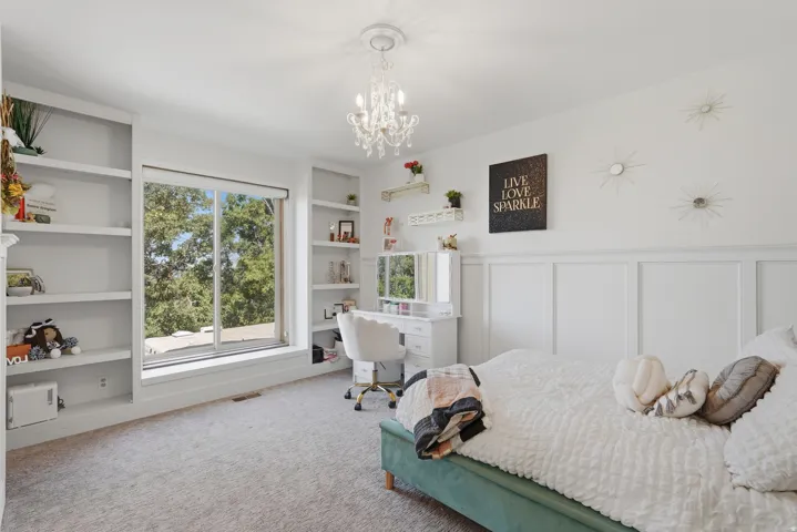 Spacious room featuring a large window, built-in shelving, wainscoting, and a decorative chandelier