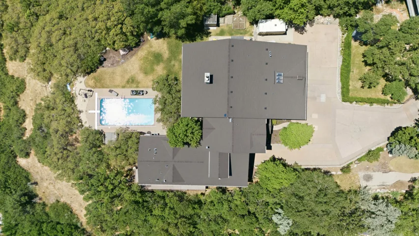 Expansive property featuring a multi-structure layout with dark gray roofing, a large inground swimming pool, and extensive surrounding greenery