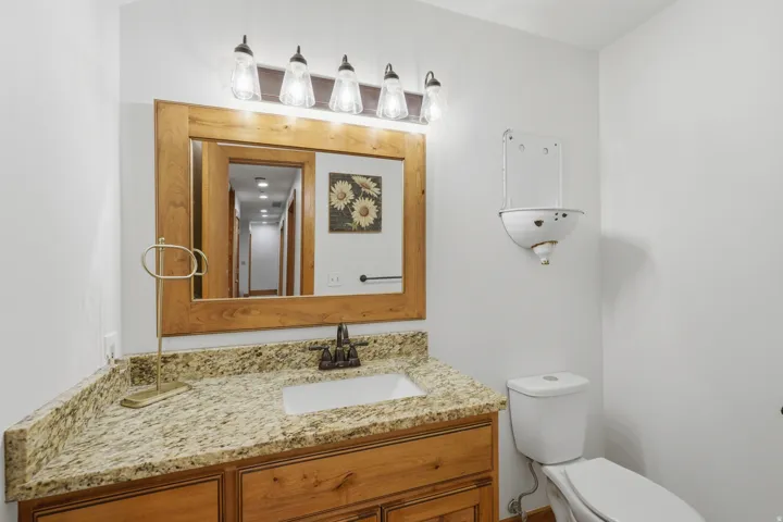 Half bath with a vanity featuring a light wood-finish frame mirror, a light granite countertop, and wood-finish cabinetry