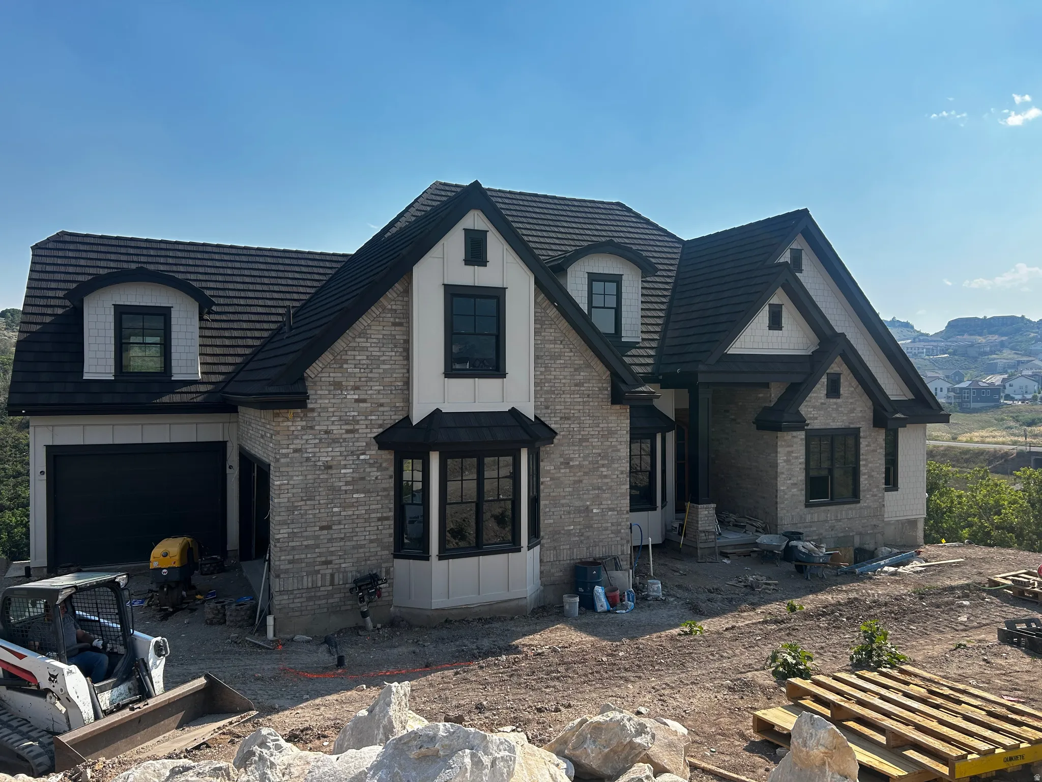 Contemporary exterior featuring light gray brick, board and batten siding, dark shingle roofing, black-framed windows, and a black garage door