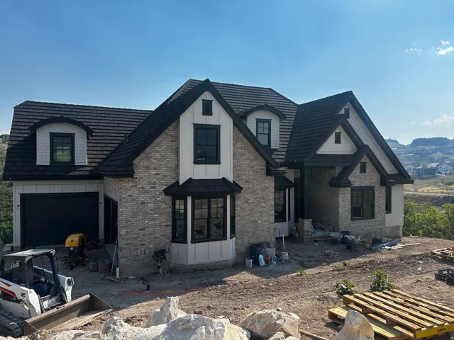 Contemporary exterior featuring light gray brick, board and batten siding, dark shingle roofing, black-framed windows, and a black garage door