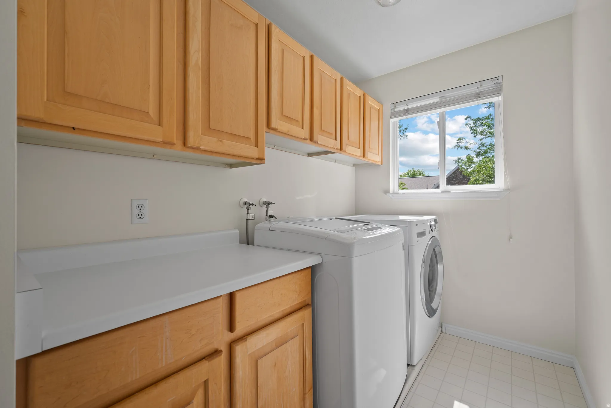 Laundry area featuring ample cabinetry, counter space, a window with natural light, and tile flooring