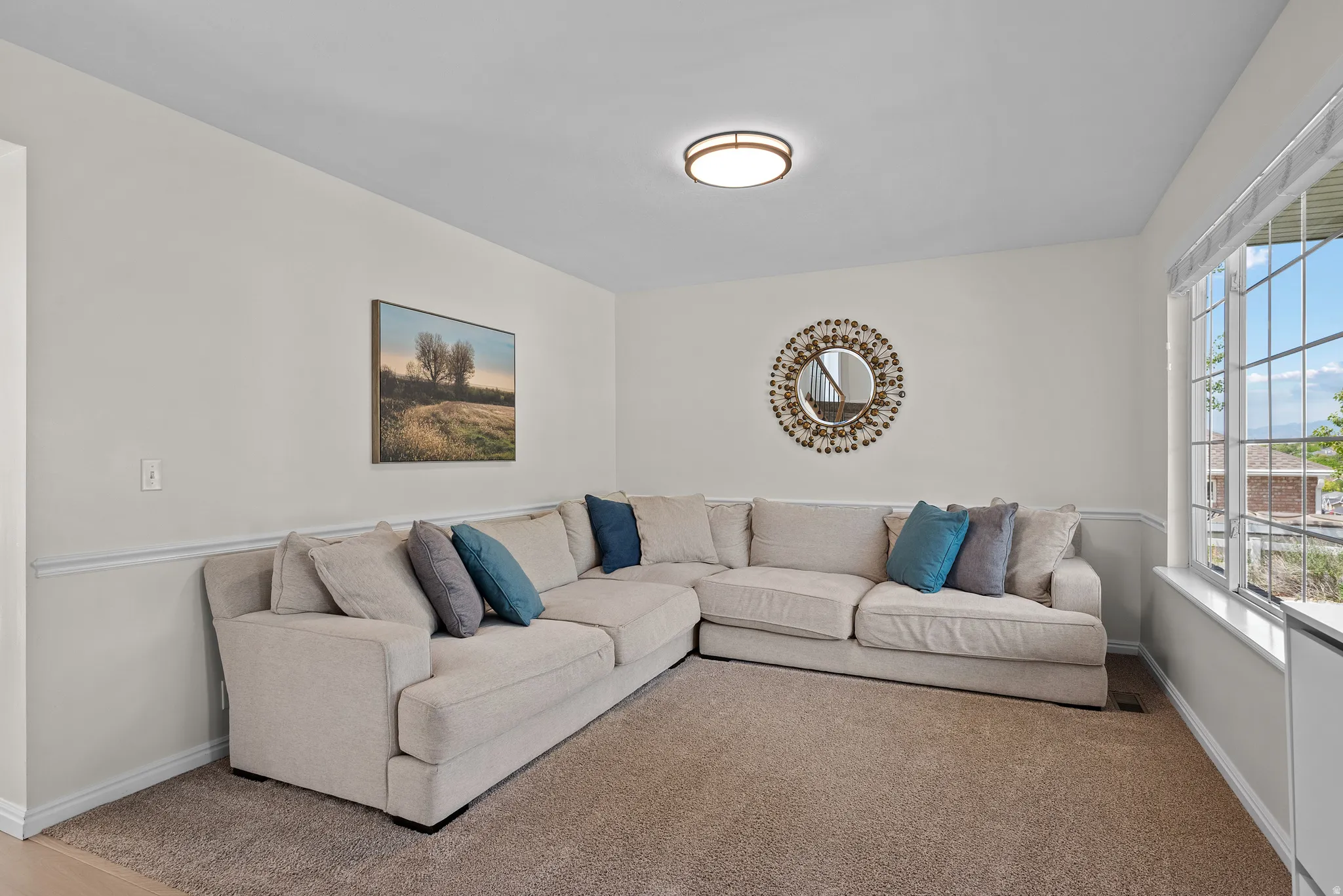 Carpeted living area featuring white walls with chair rail molding, a large multi-pane window, and a flush-mount ceiling light fixture