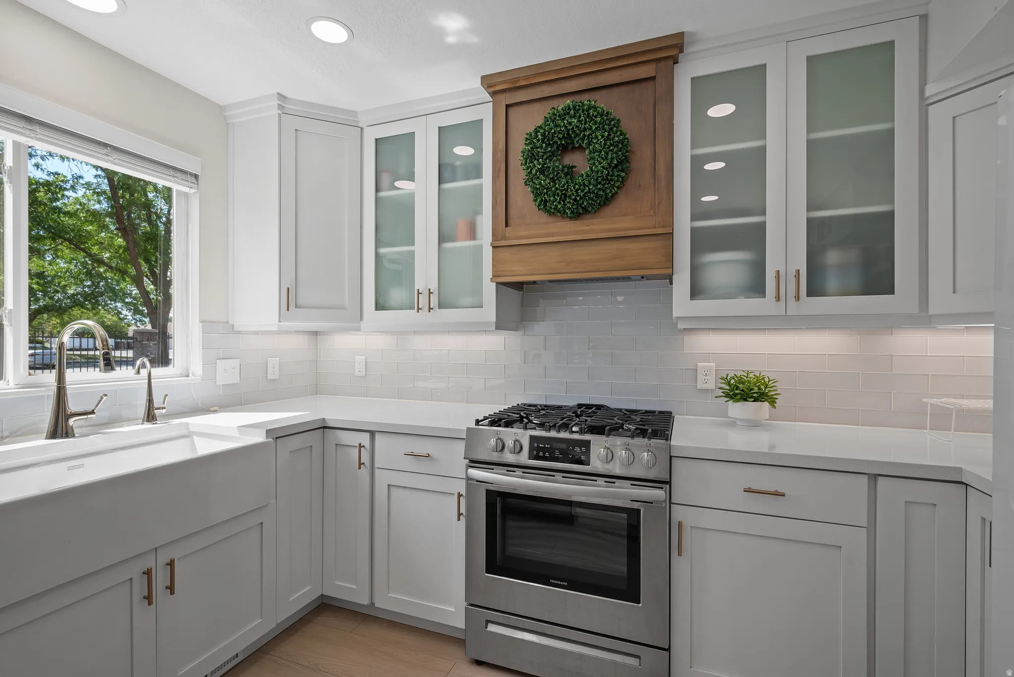Bright kitchen featuring white shaker cabinetry, an integrated farmhouse sink, stainless steel range, and a subway tile backsplash