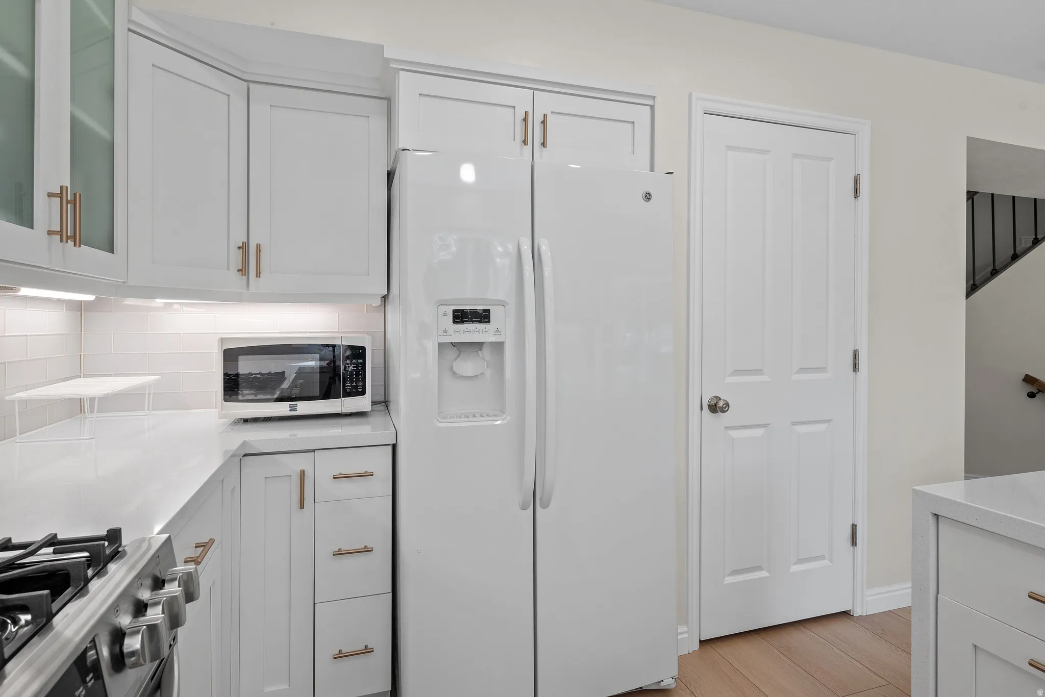 Modern kitchen featuring white cabinetry, light countertops, subway tile backsplash, and wood-finish flooring