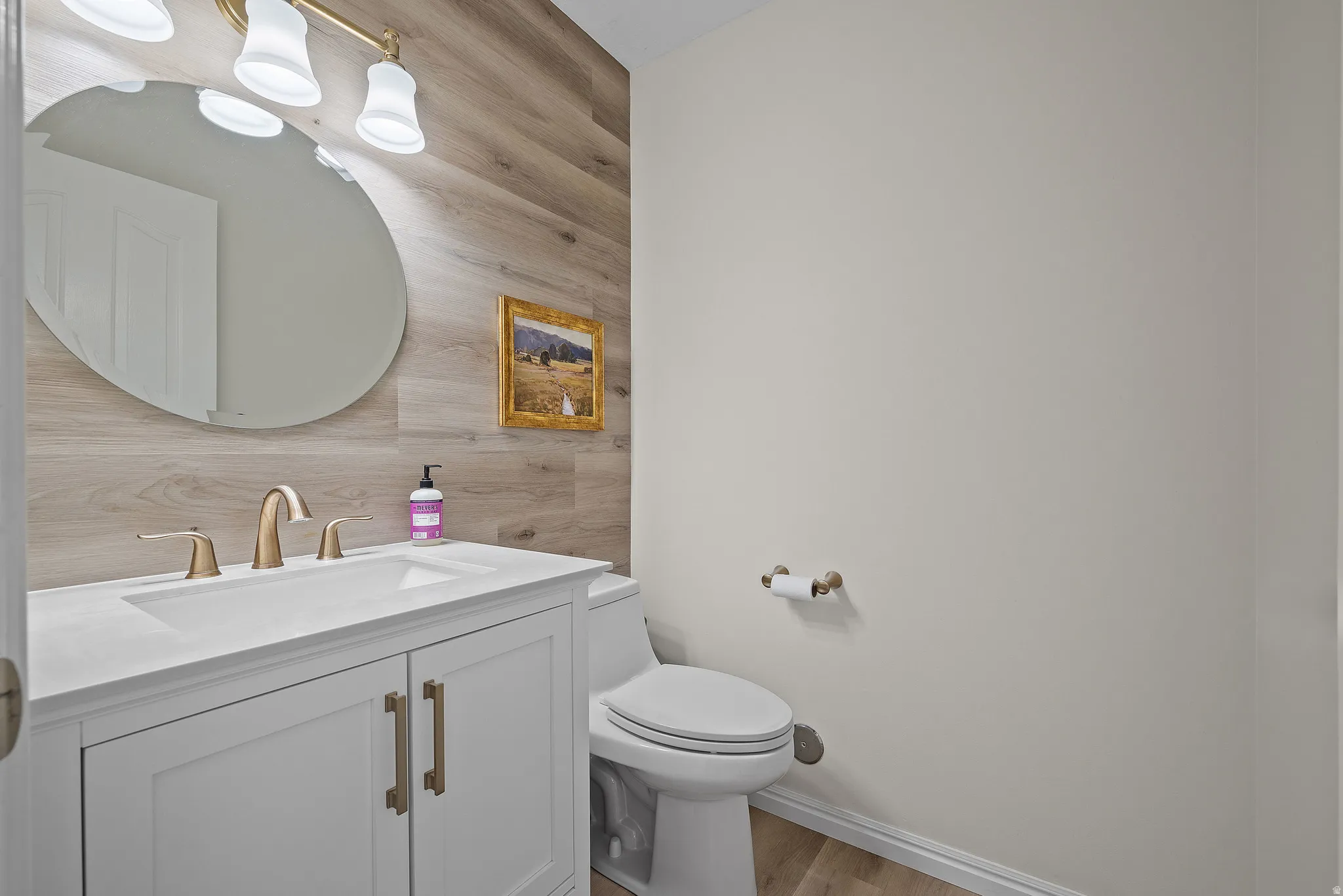 Bathroom featuring a white vanity with an integrated sink, brushed gold hardware, and a wood-finish accent wall