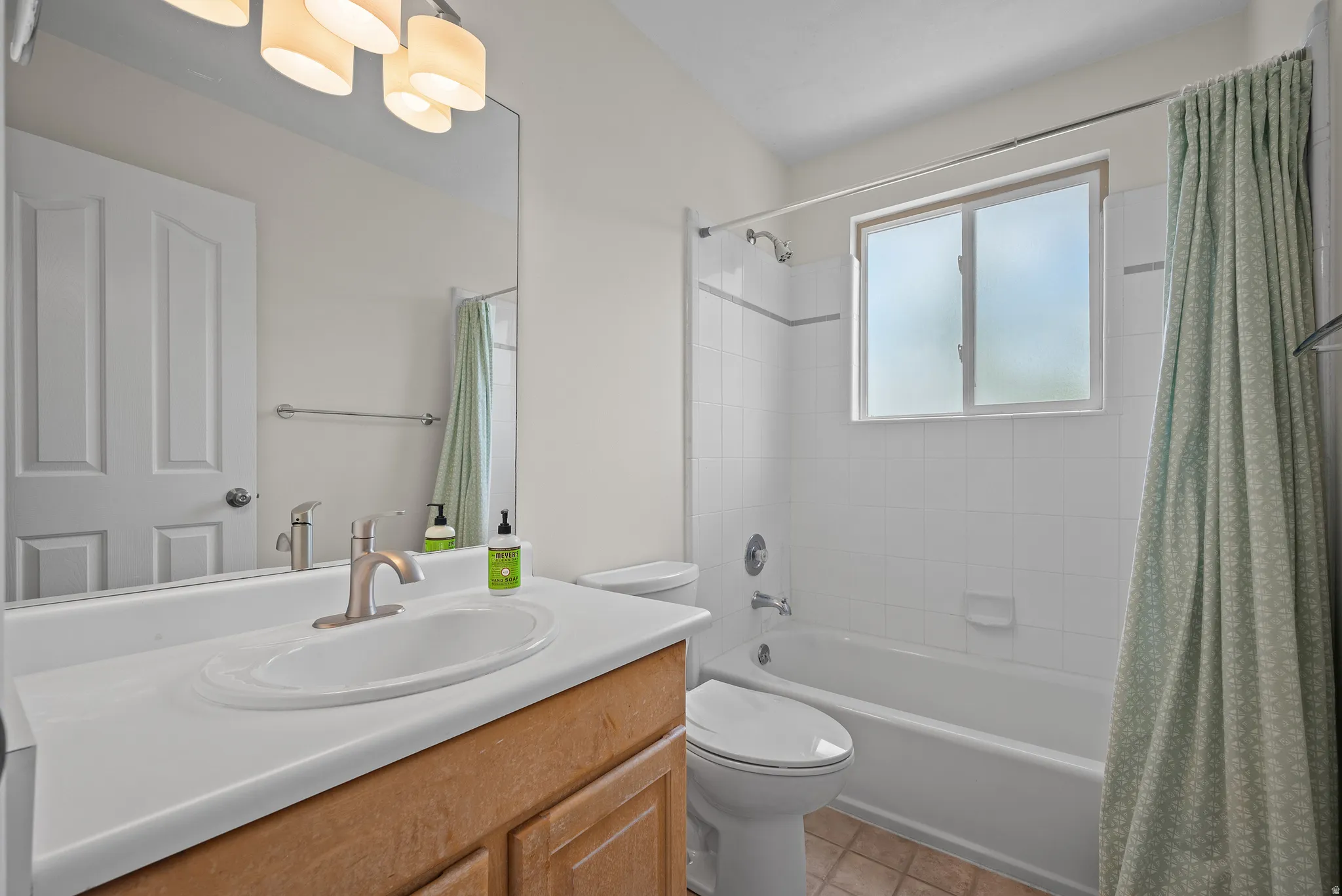 Bathroom featuring a light wood-finish vanity with an integrated sink, brushed nickel faucet, full-width mirror, and a three-light vanity fixture