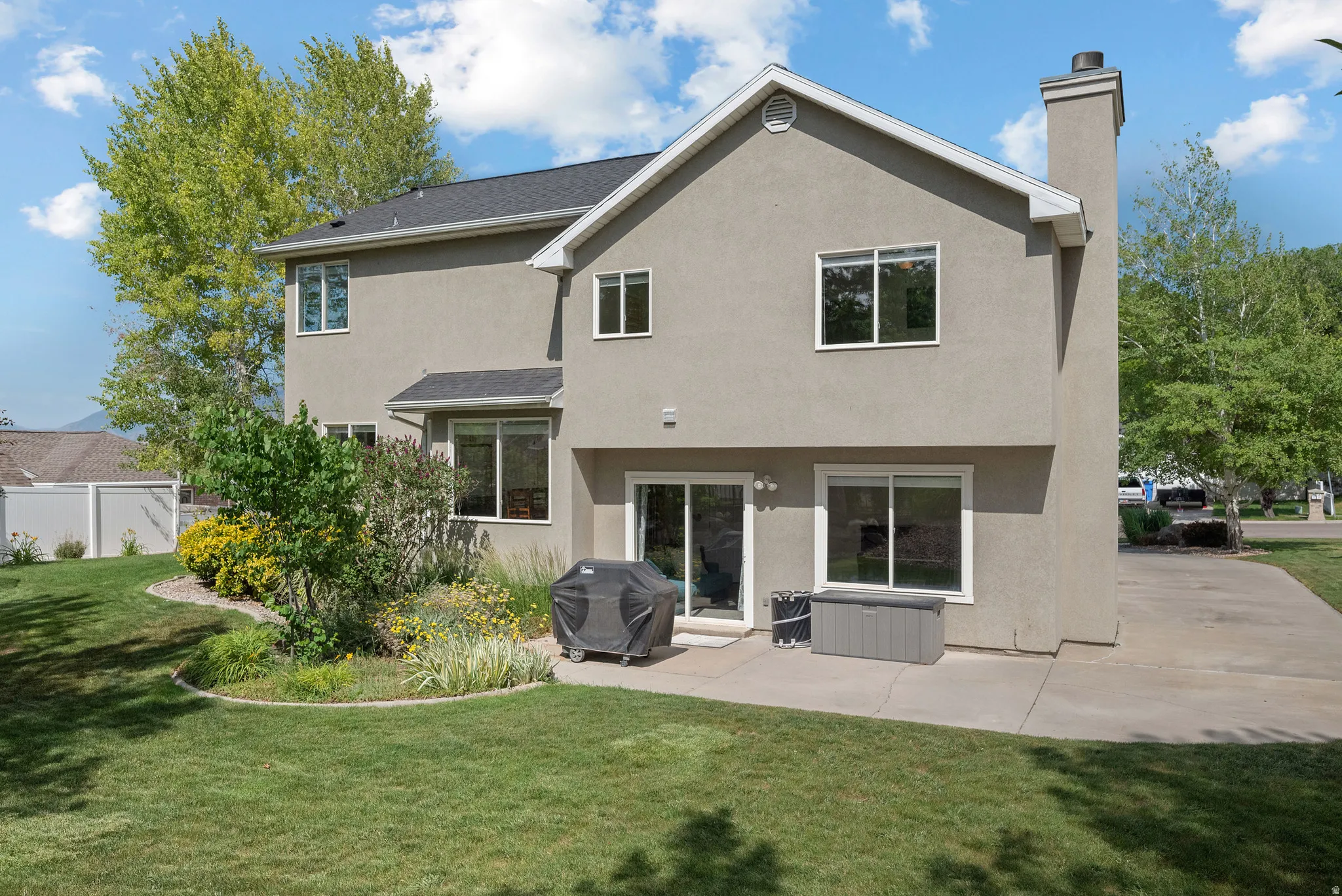 Rear exterior featuring stucco siding, a dark shingle roof, a concrete patio, and a grass lawn with landscaping