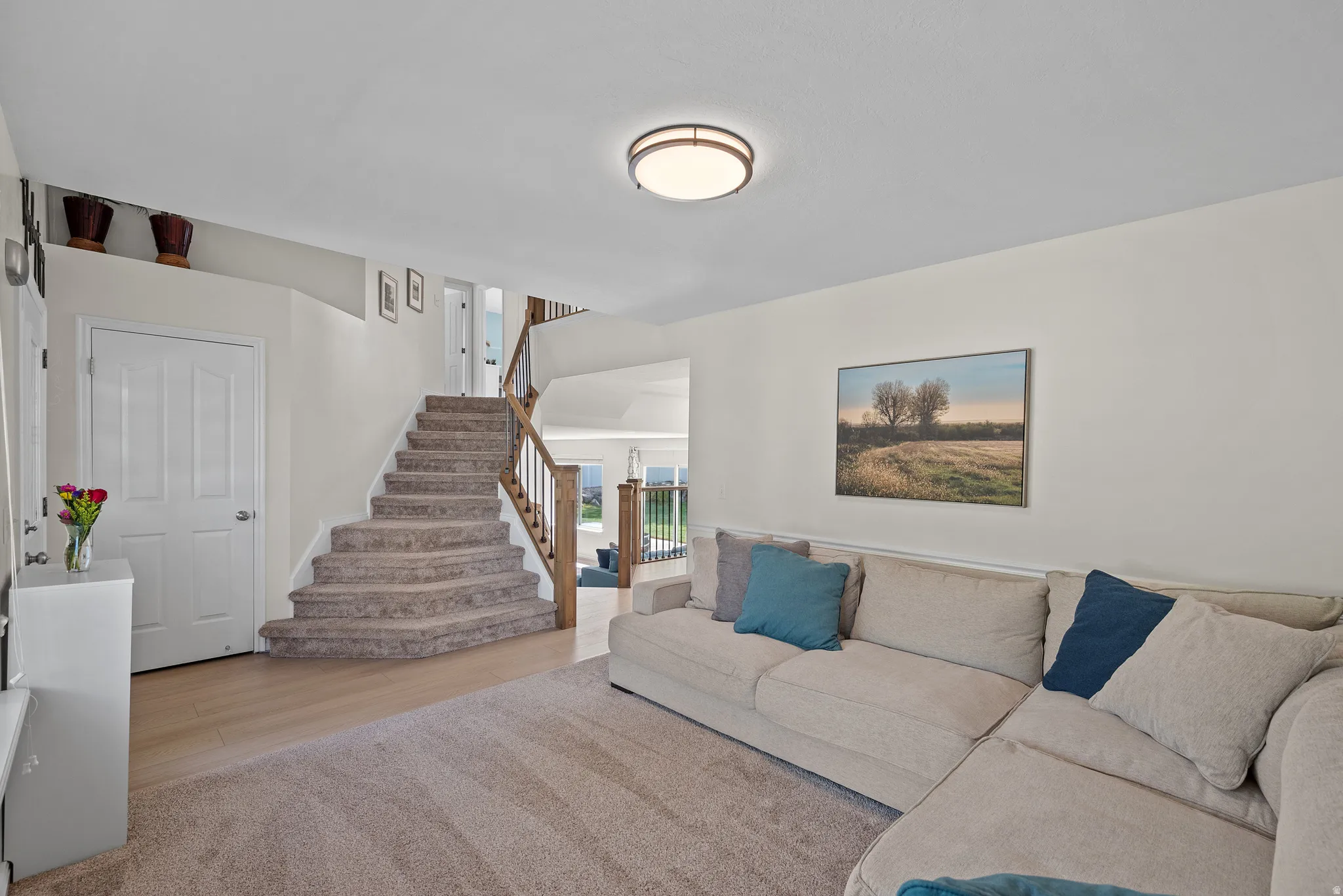 Inviting living space featuring a carpeted staircase with wood railing, warm wood-finish flooring, and a large area rug