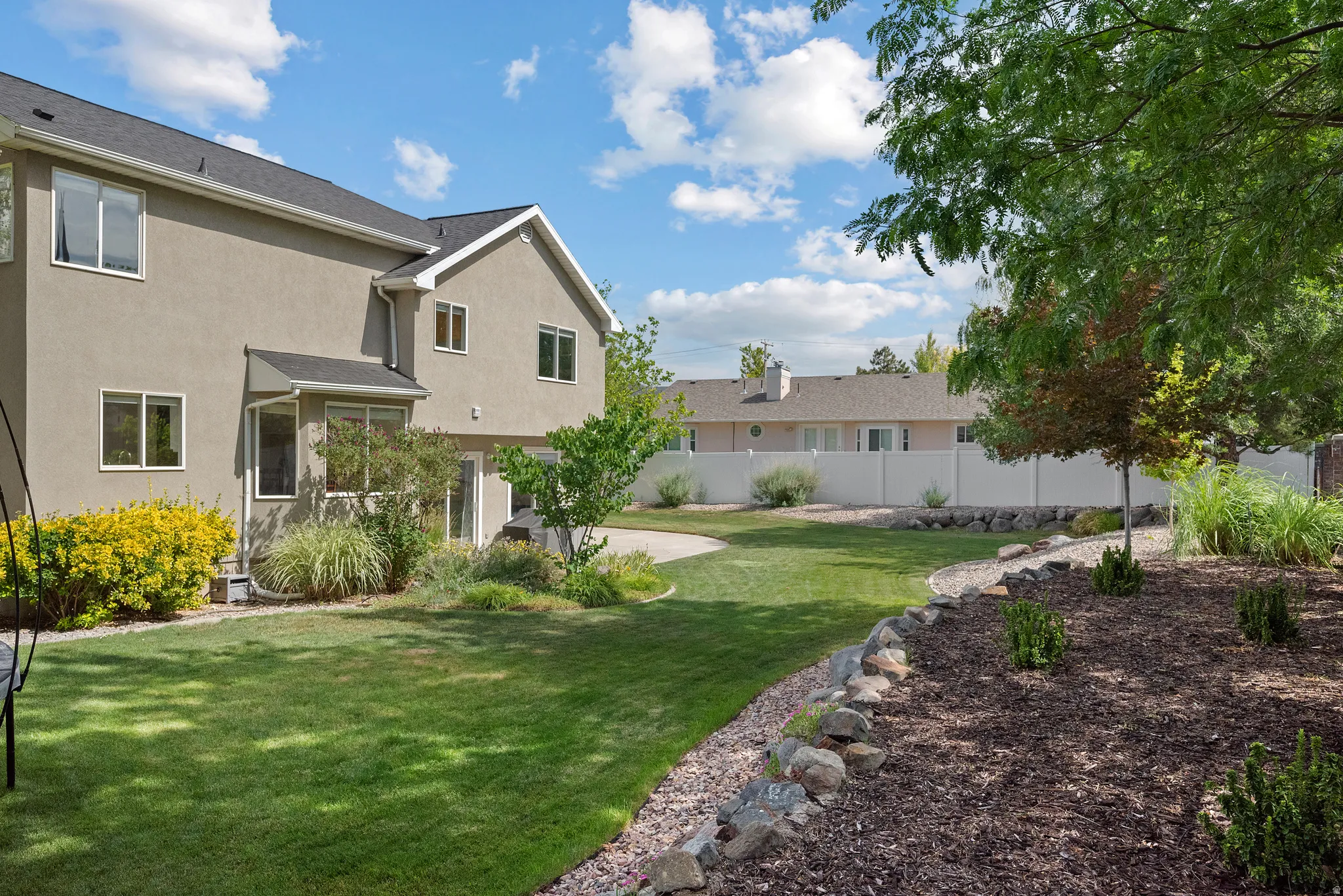 Expansive backyard featuring a manicured lawn, established landscaping beds with decorative rock borders, and mature trees providing natural shade