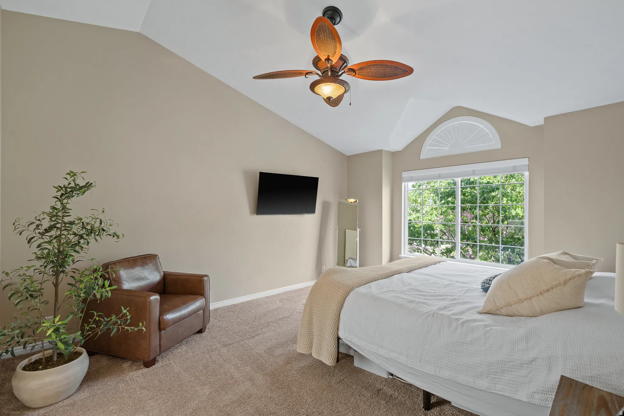 Arched window with transom above, vaulted ceiling, ceiling fan with light fixture, mounted television, and carpet flooring