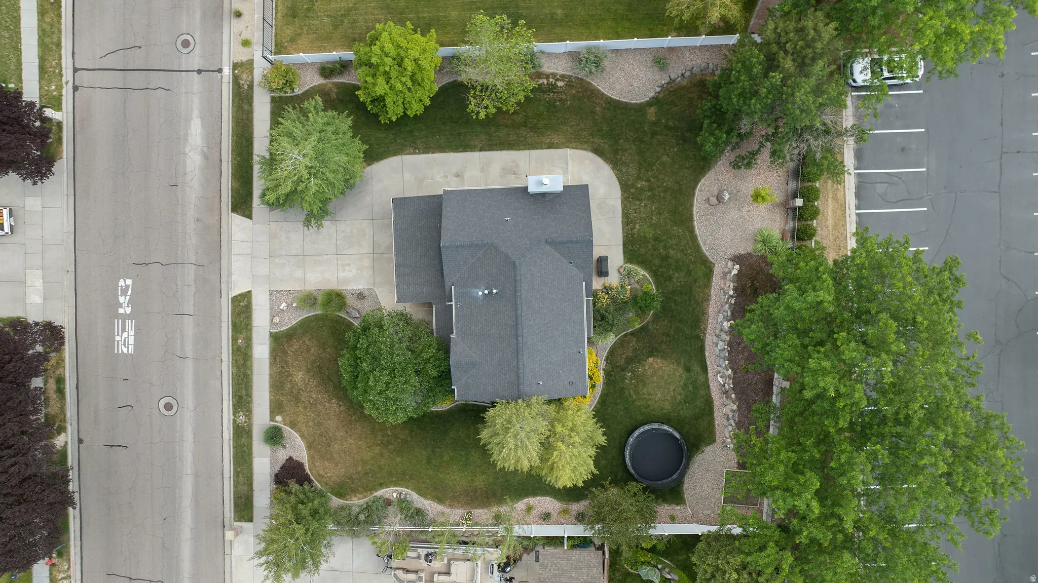 Well-maintained grounds featuring a dark shingle roof, established landscaping, a concrete driveway, and mature trees
