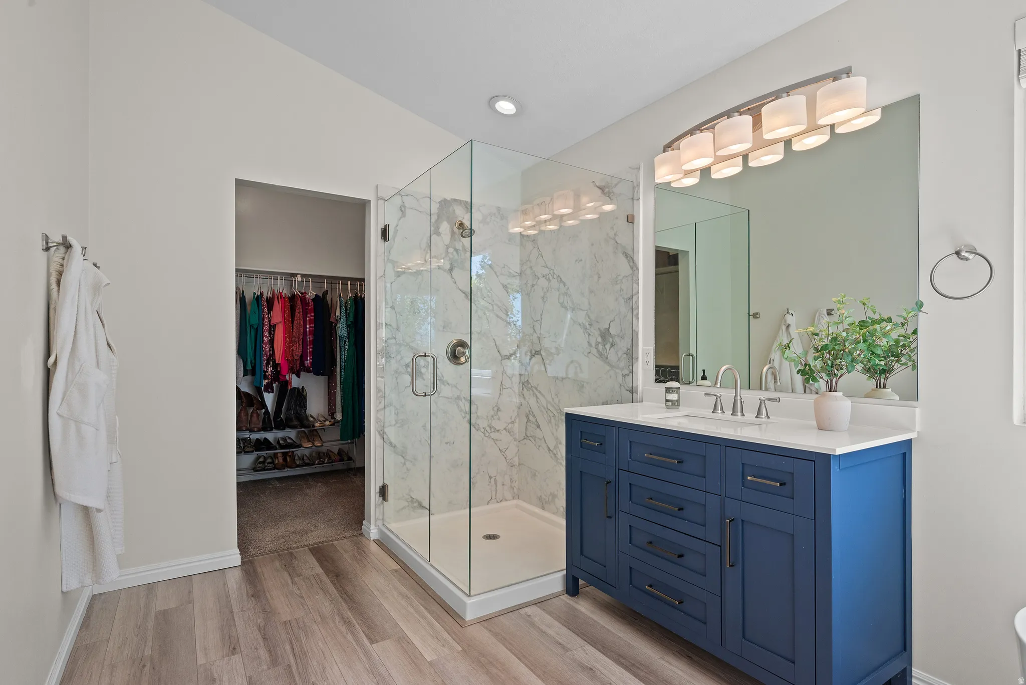 Modern bathroom featuring a glass-enclosed shower with marble-look tile, a blue vanity with a white countertop and integrated sink, and wood-finish flooring
