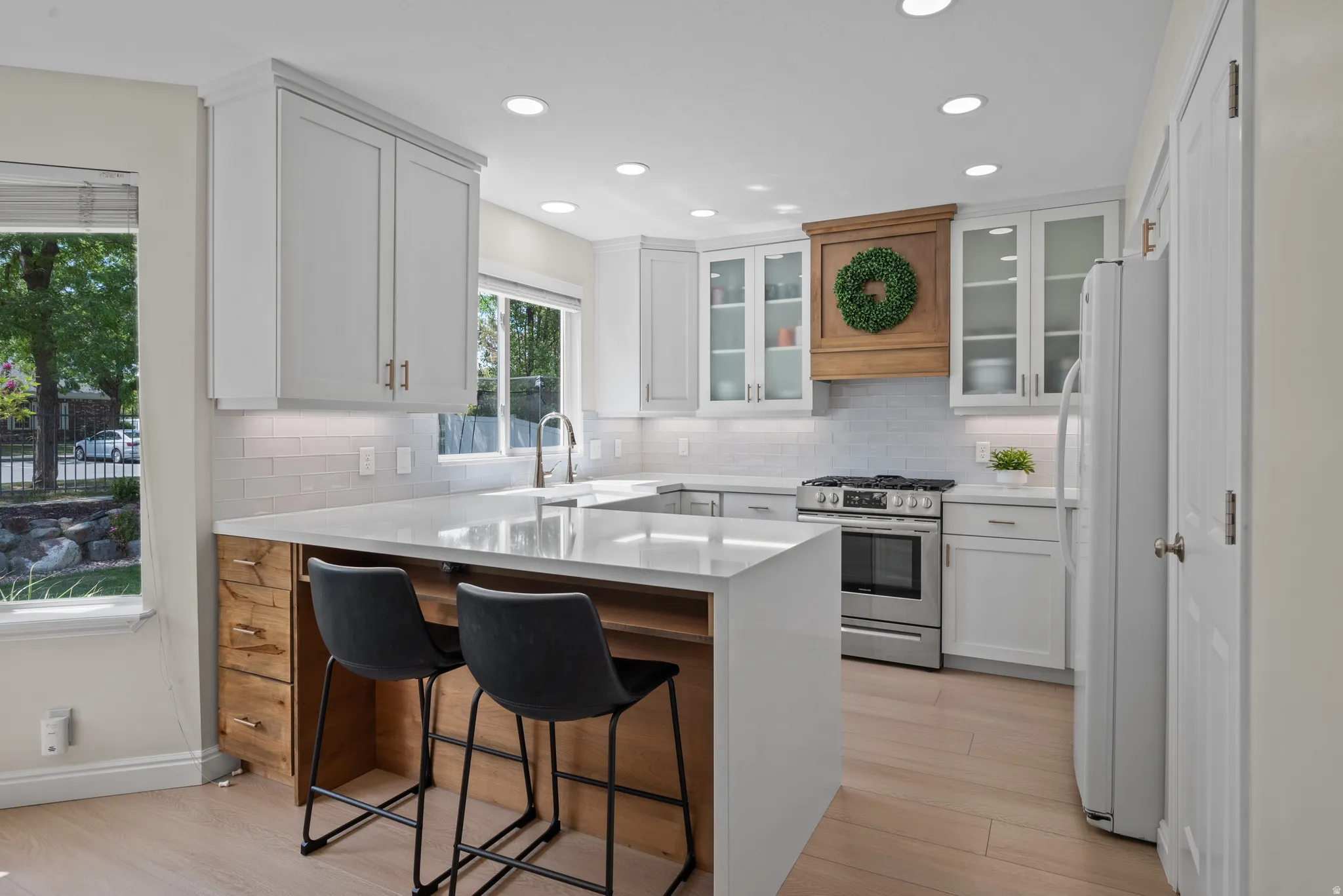 Modern kitchen featuring an island with wood-finish paneling and seating, light wood-finish flooring, white perimeter cabinetry, stainless steel range, and a wood-finish range hood