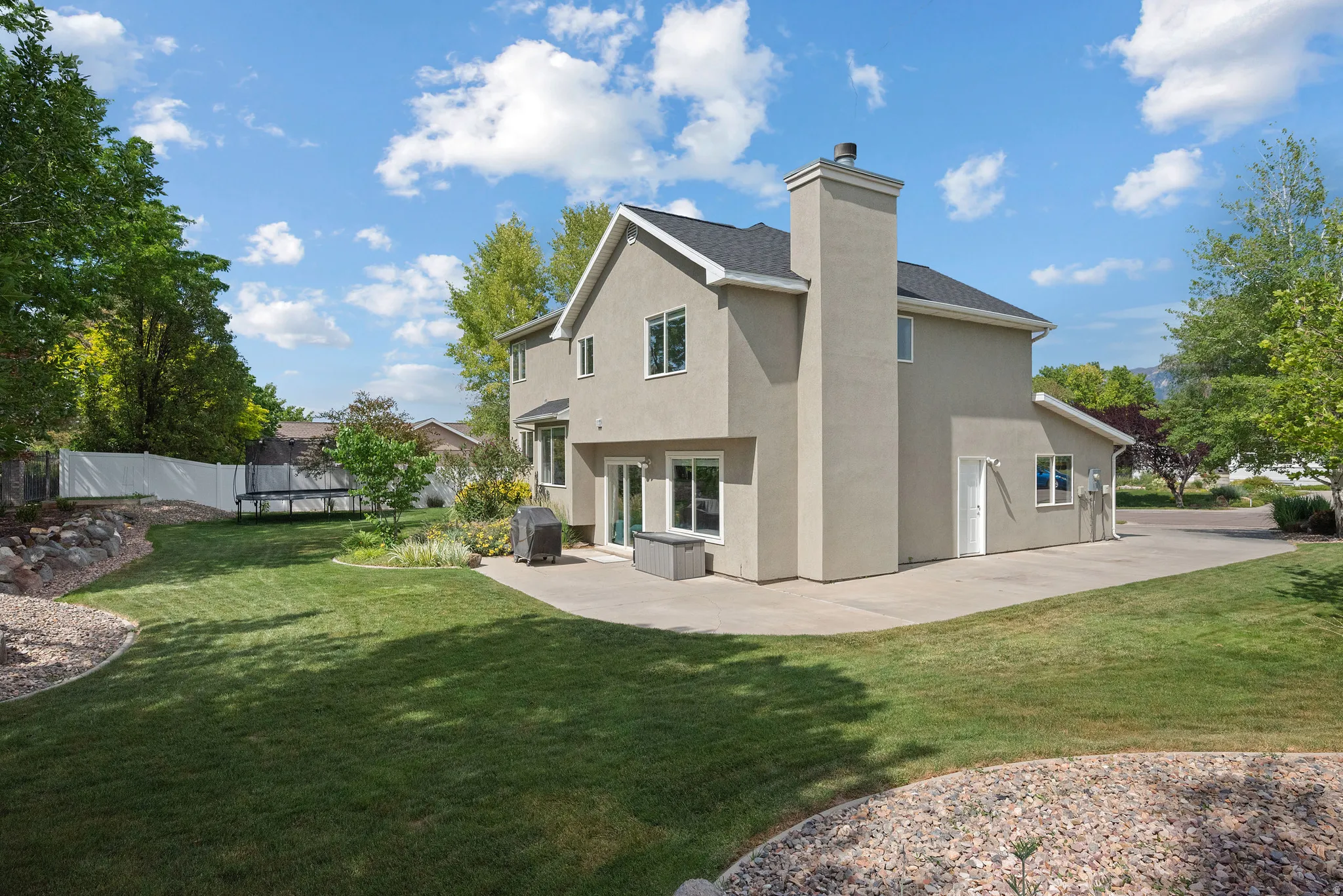 Stucco exterior residence featuring a dark shingle roof, a prominent chimney, and multiple windows