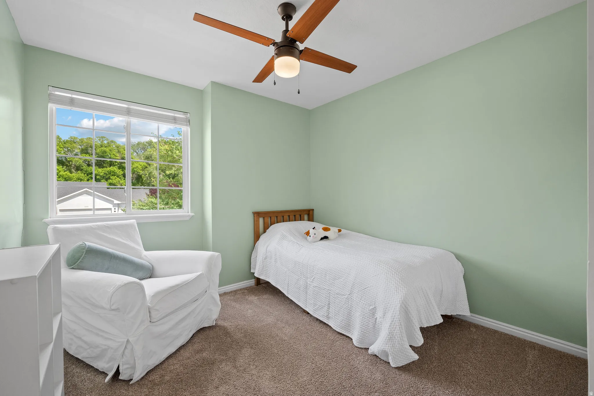 Carpeted room featuring light green walls, a white window frame, and a ceiling fan with wood-finish blades and an integrated light fixture