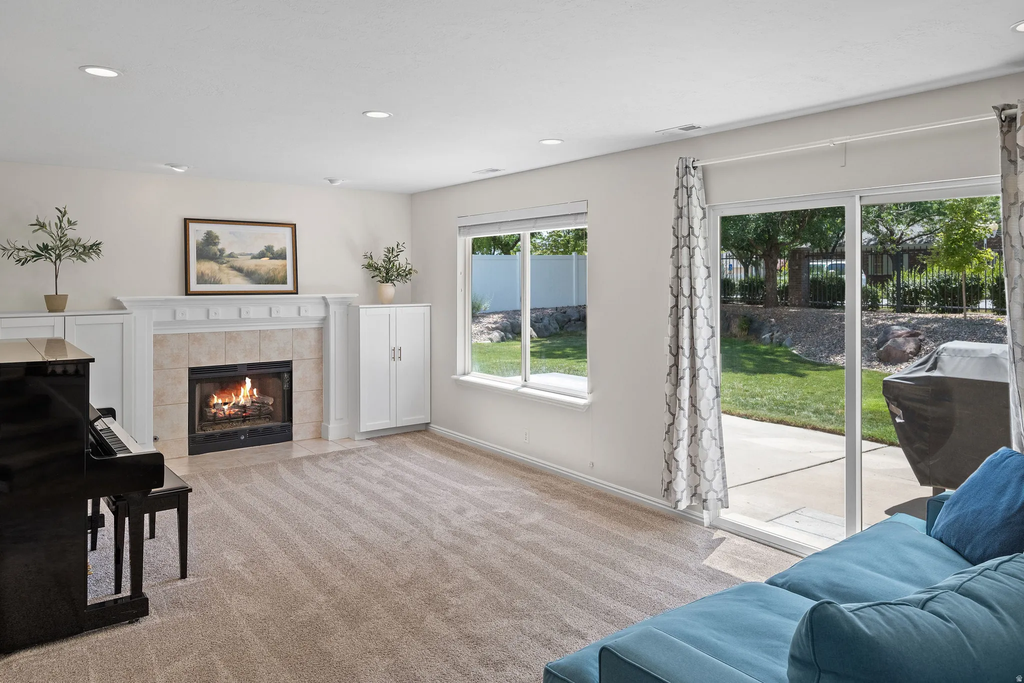 Living area featuring a central fireplace with a tiled surround and white mantel, built-in cabinetry, recessed lighting, and carpet flooring