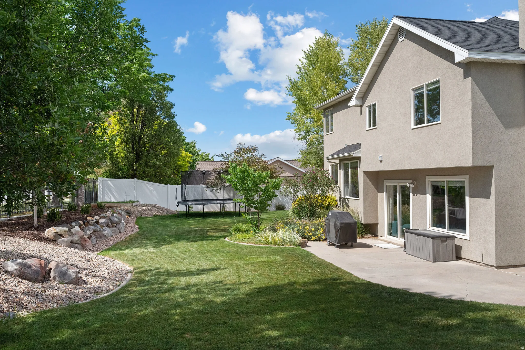 Spacious backyard featuring a manicured lawn, established perimeter trees, and a rock retaining wall with gravel landscaping