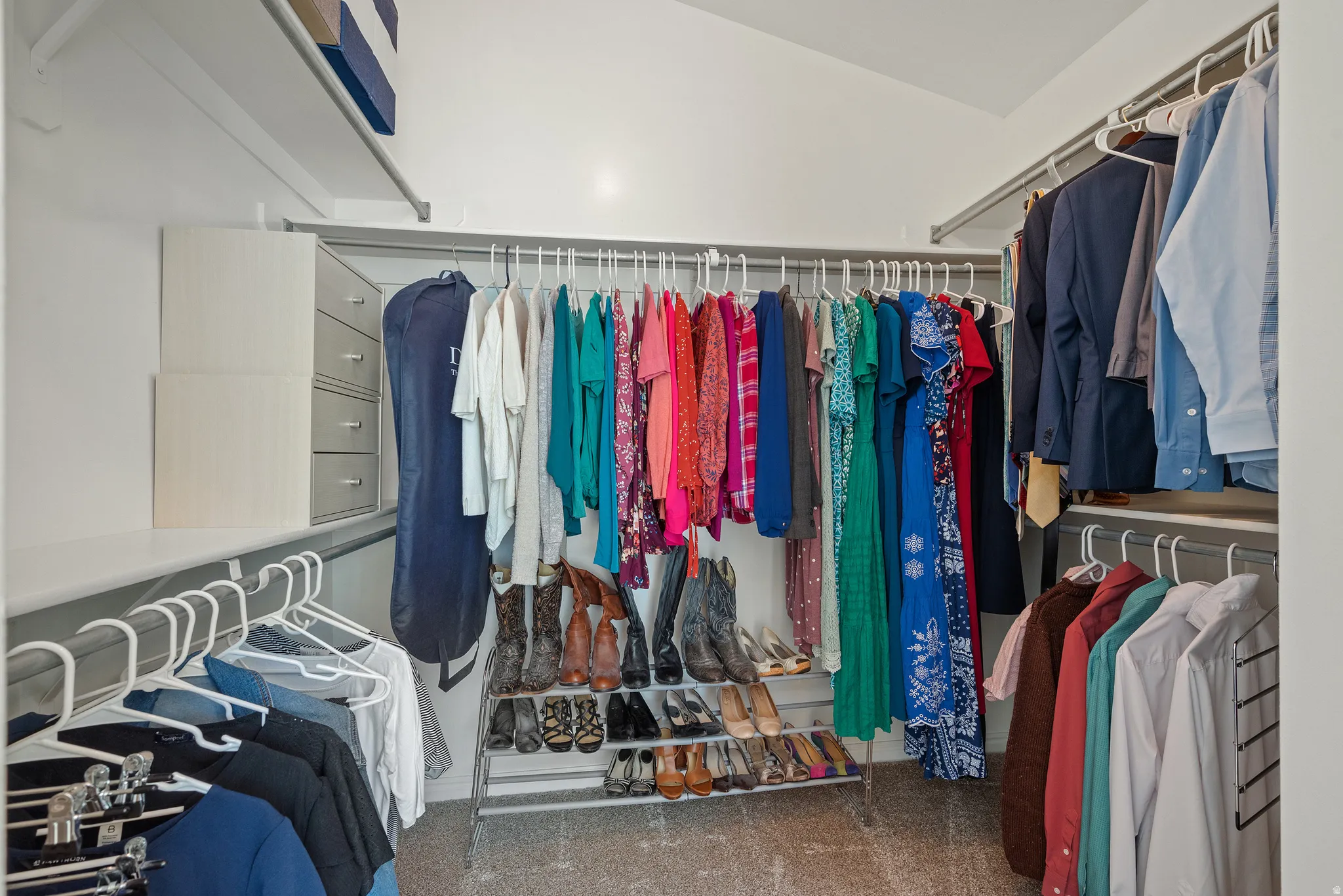 Walk-in closet featuring extensive built-in shelving, multiple hanging rods, integrated drawer units, and textured carpeting