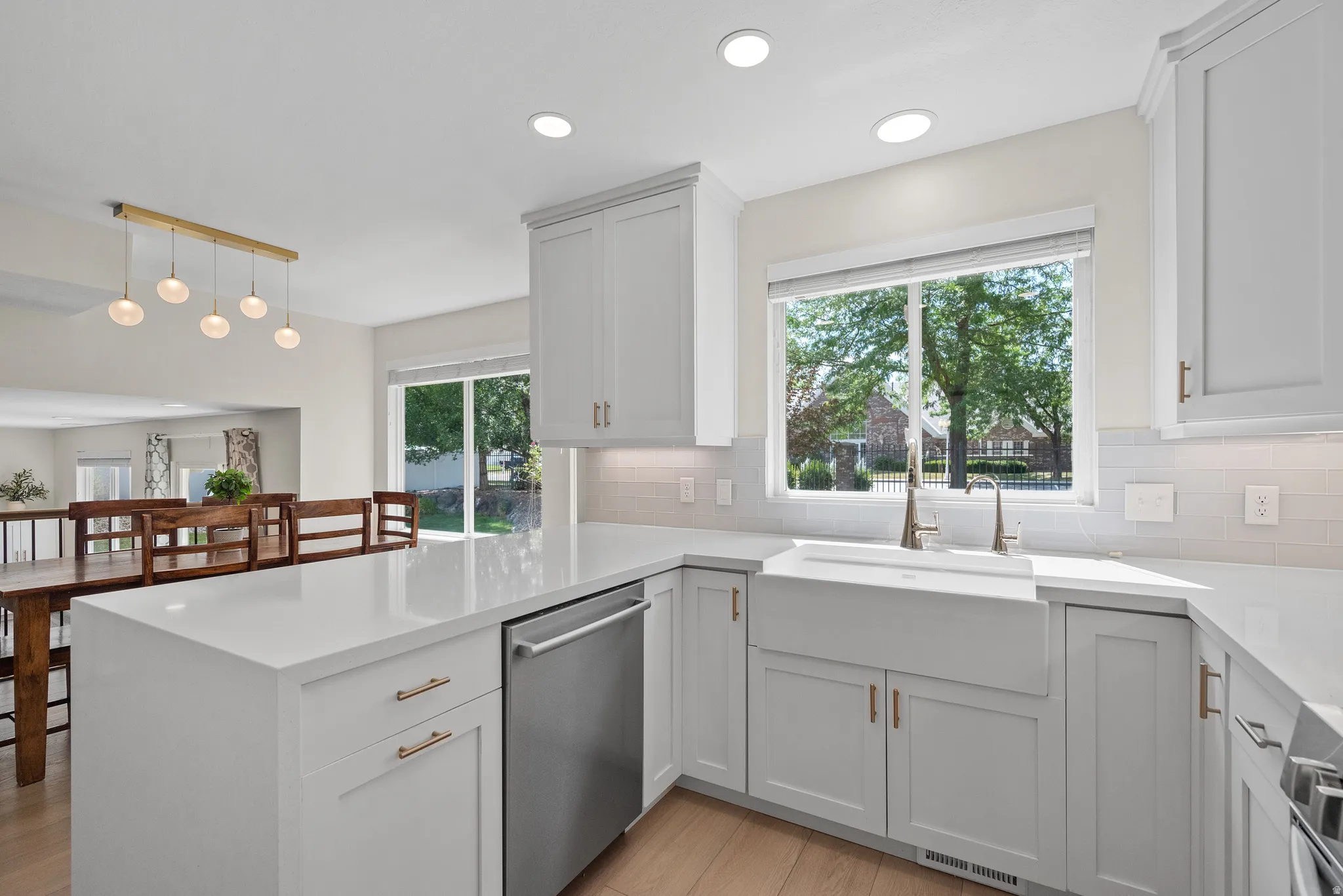 Modern kitchen featuring white shaker cabinetry, light countertops, wood-finish flooring, stainless steel dishwasher, and a farmhouse sink with a contemporary faucet