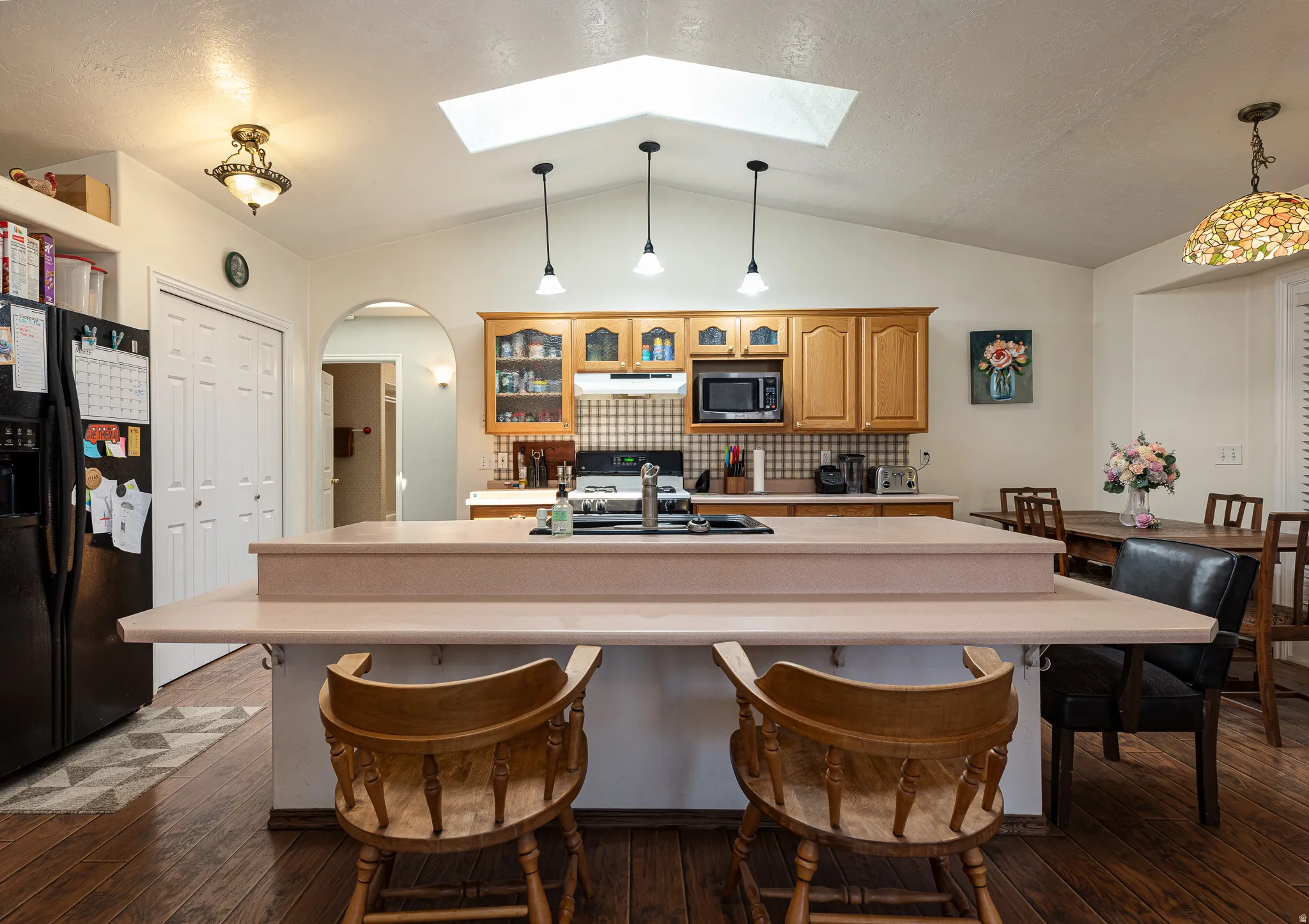 Kitchen featuring a central island with counter seating, wood flooring, a vaulted ceiling with a skylight, pendant lighting, and light wood cabinetry