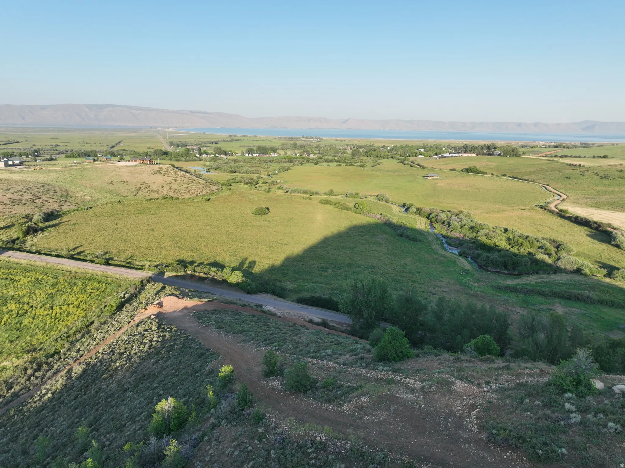 Expansive green landscape featuring a distant body of water, rolling hills, a meandering stream, and scattered trees