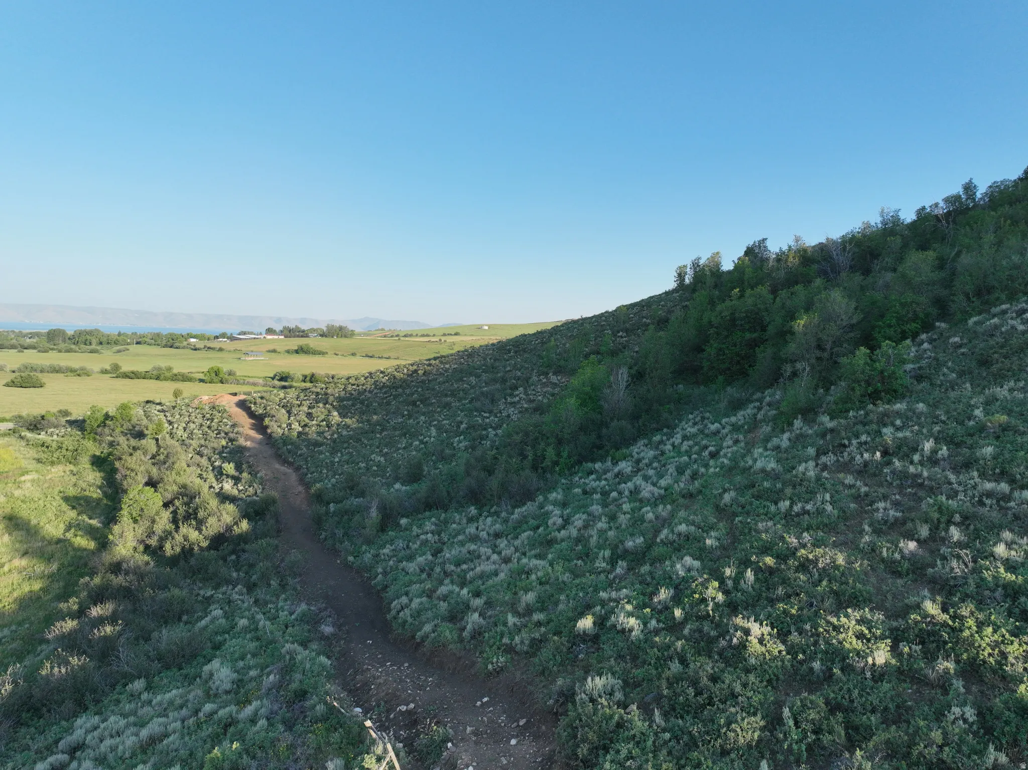 Expansive sloping terrain with natural vegetation and distant water body
