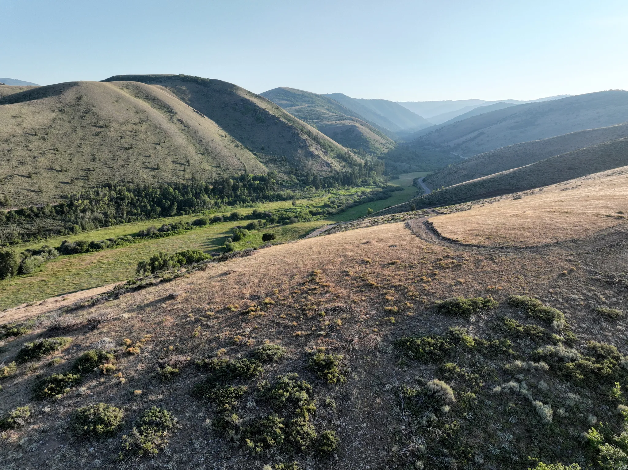 Expansive mountain landscape featuring a winding valley and a visible path across the hillside